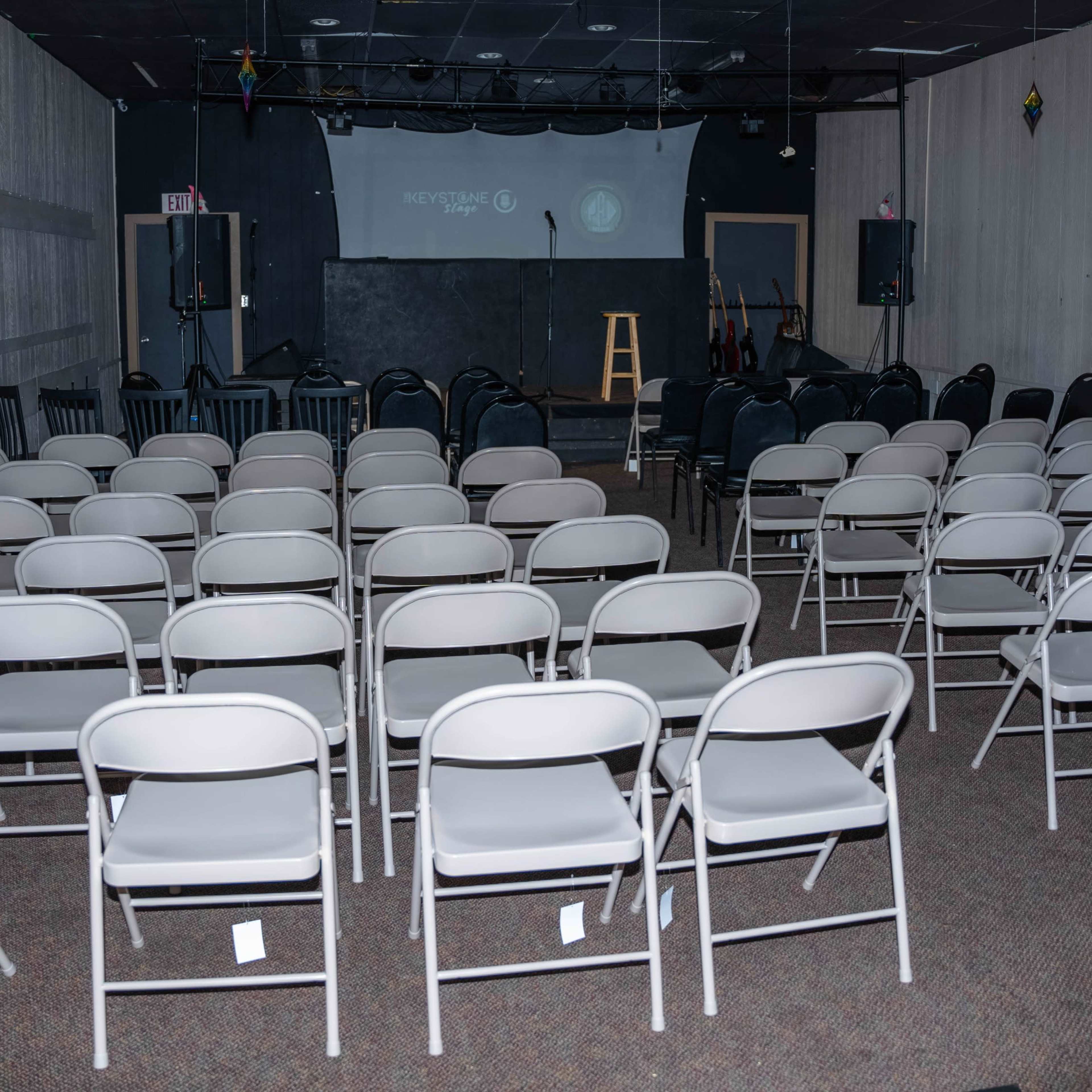 An empty performance space set up with rows of white folding chairs facing a small stage.
