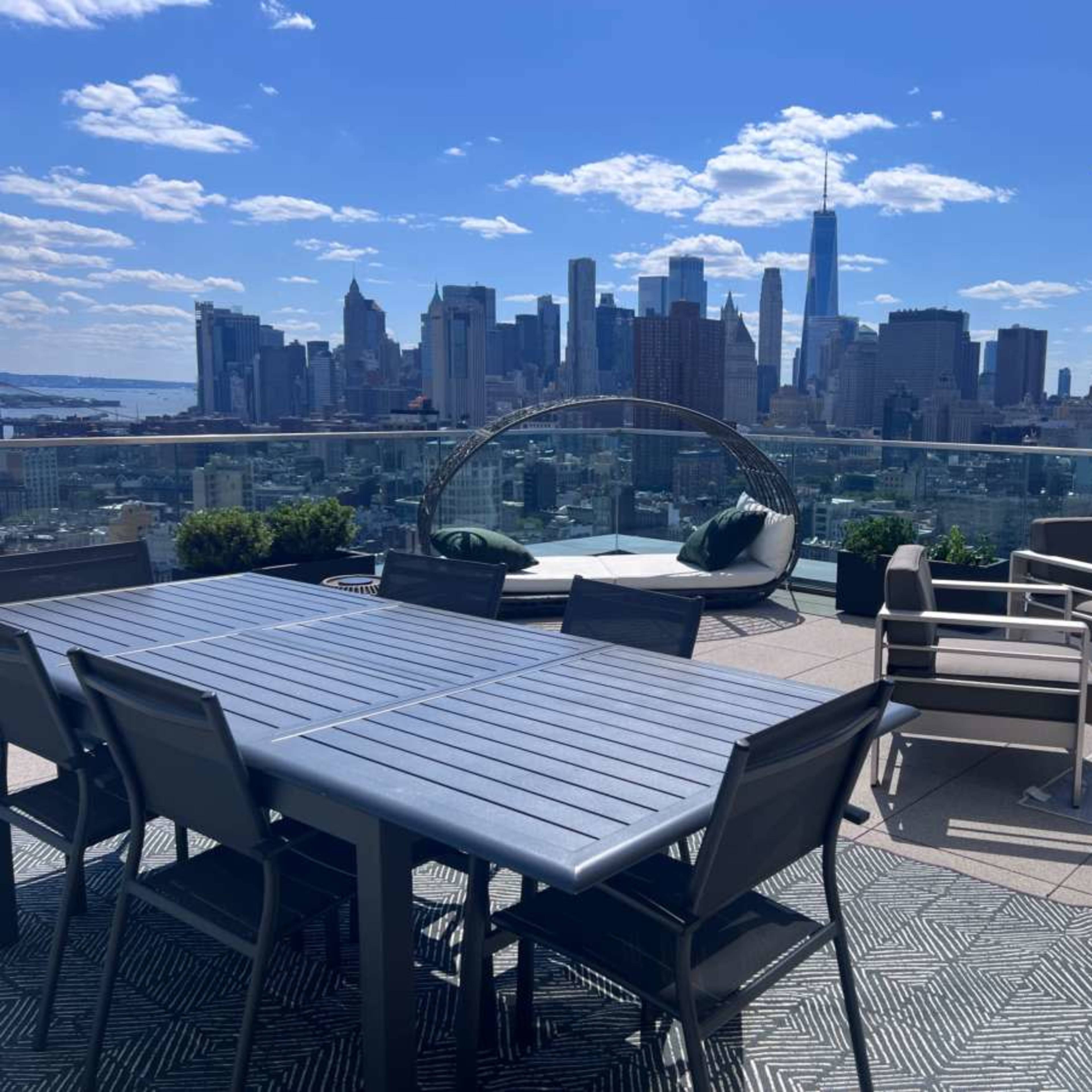 A rooftop terrace features modern outdoor furniture with a view of the New York City skyline.