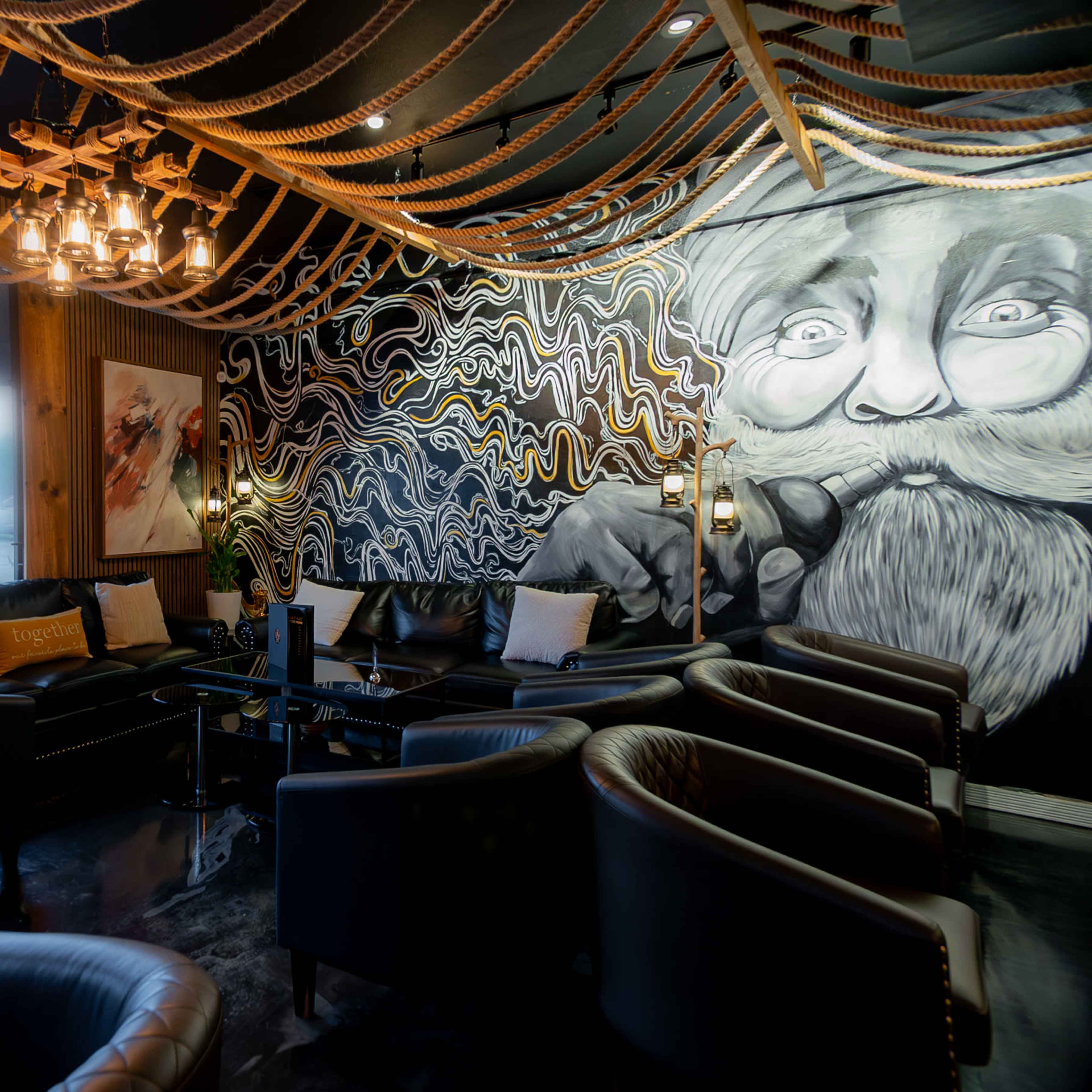A lounge area with leather seating, a mural of a bearded man on the wall, and decorative rope lighting.