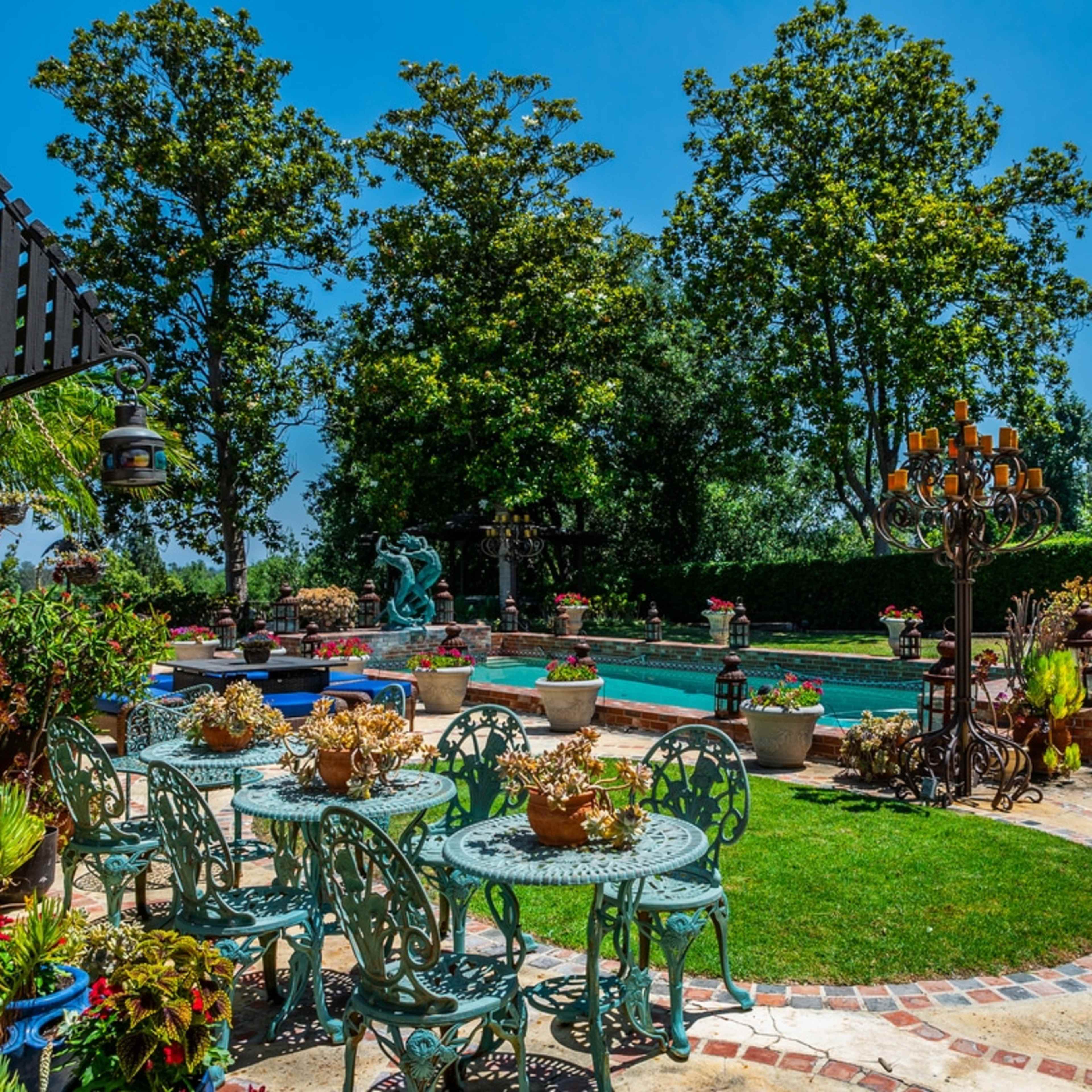 A garden area with a swimming pool, surrounded by trees and decorated with various plants, sculptures, and outdoor furniture.