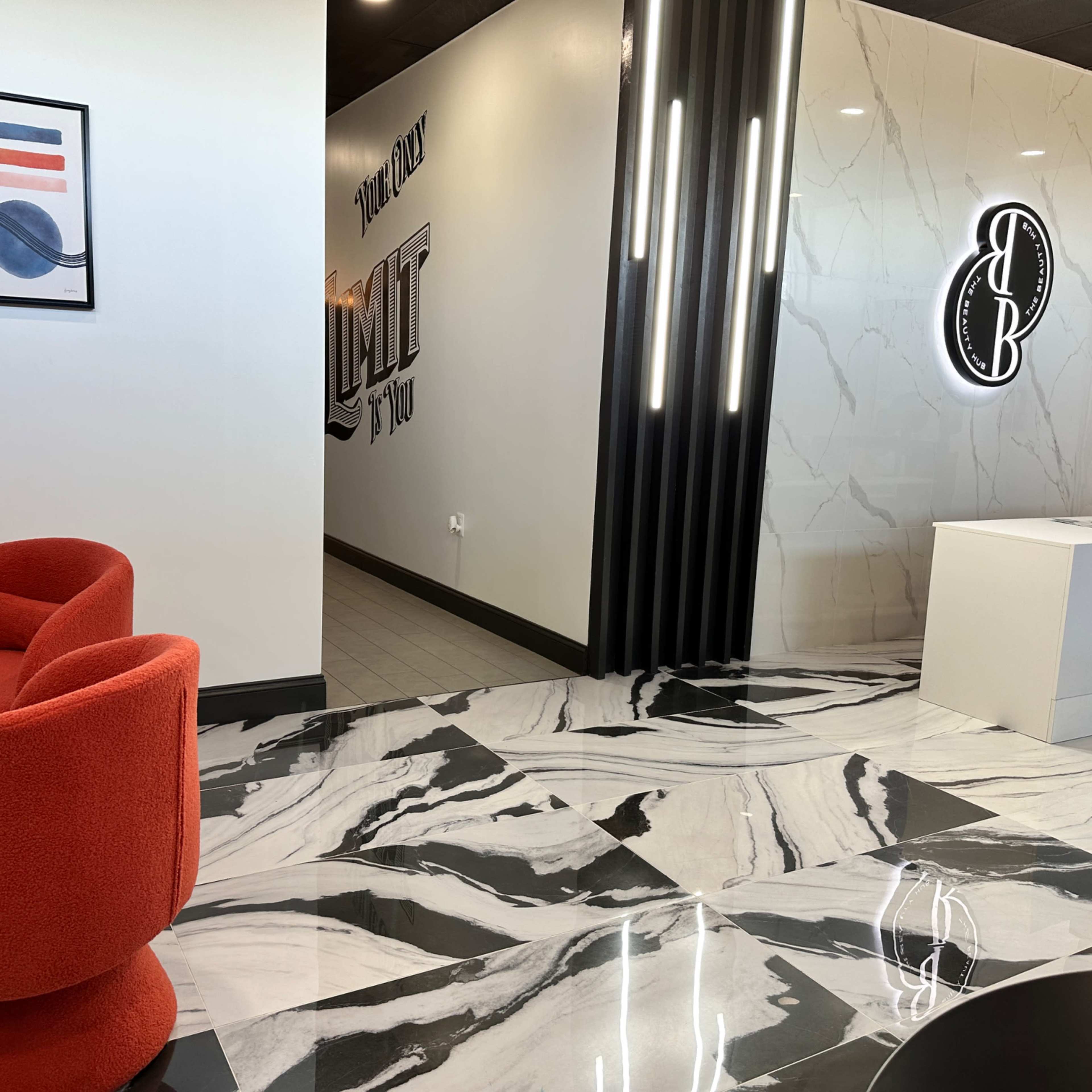 A modern interior design featuring a reception area with a red chair, a marble floor, and a decorative wall with illuminated signage.