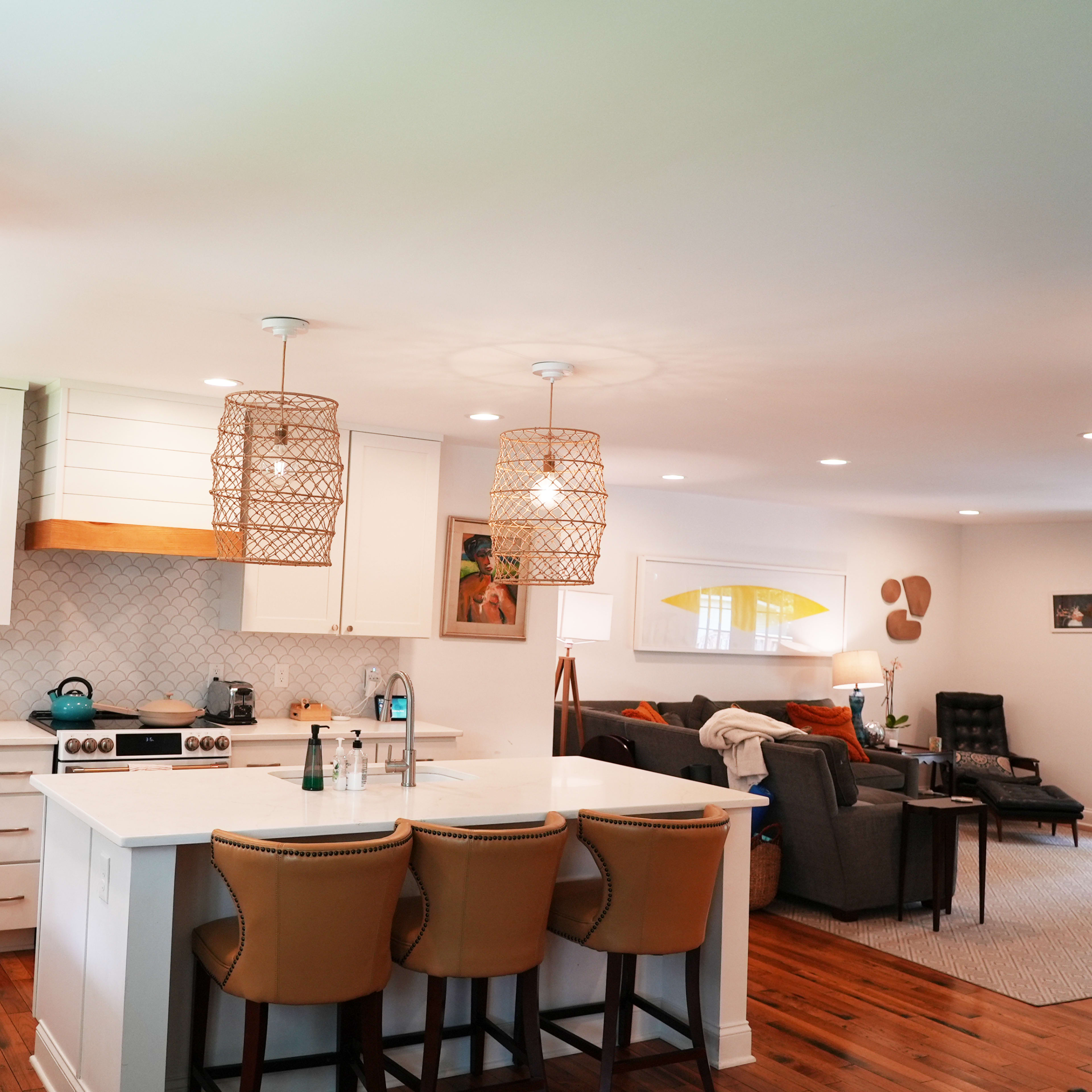 A modern kitchen with white cabinets, a large island with seating, and a living area in the background featuring a sofa and armchairs.