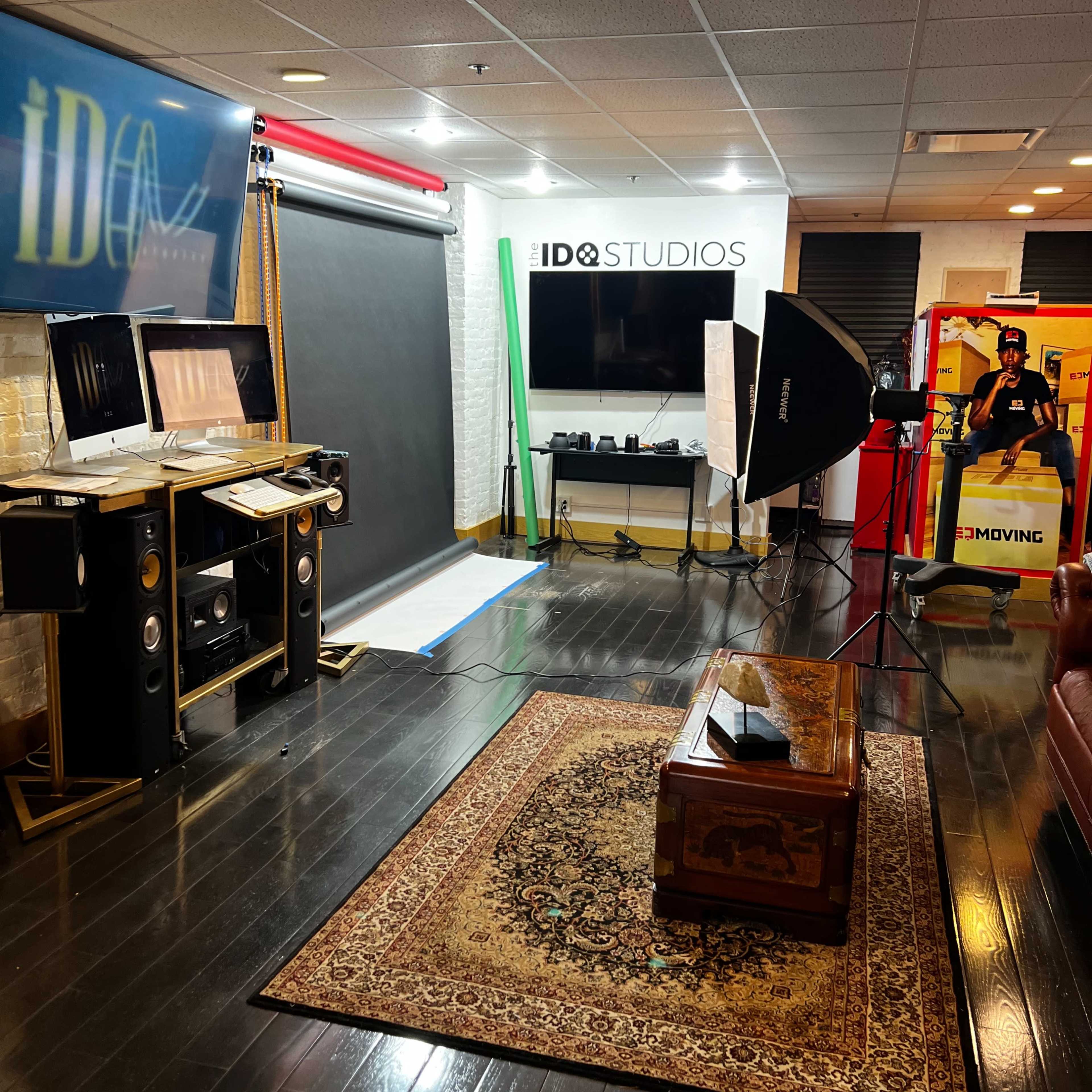 A photography studio setup with a backdrop, lighting equipment, and various props, along with a sofa and decorative rug.