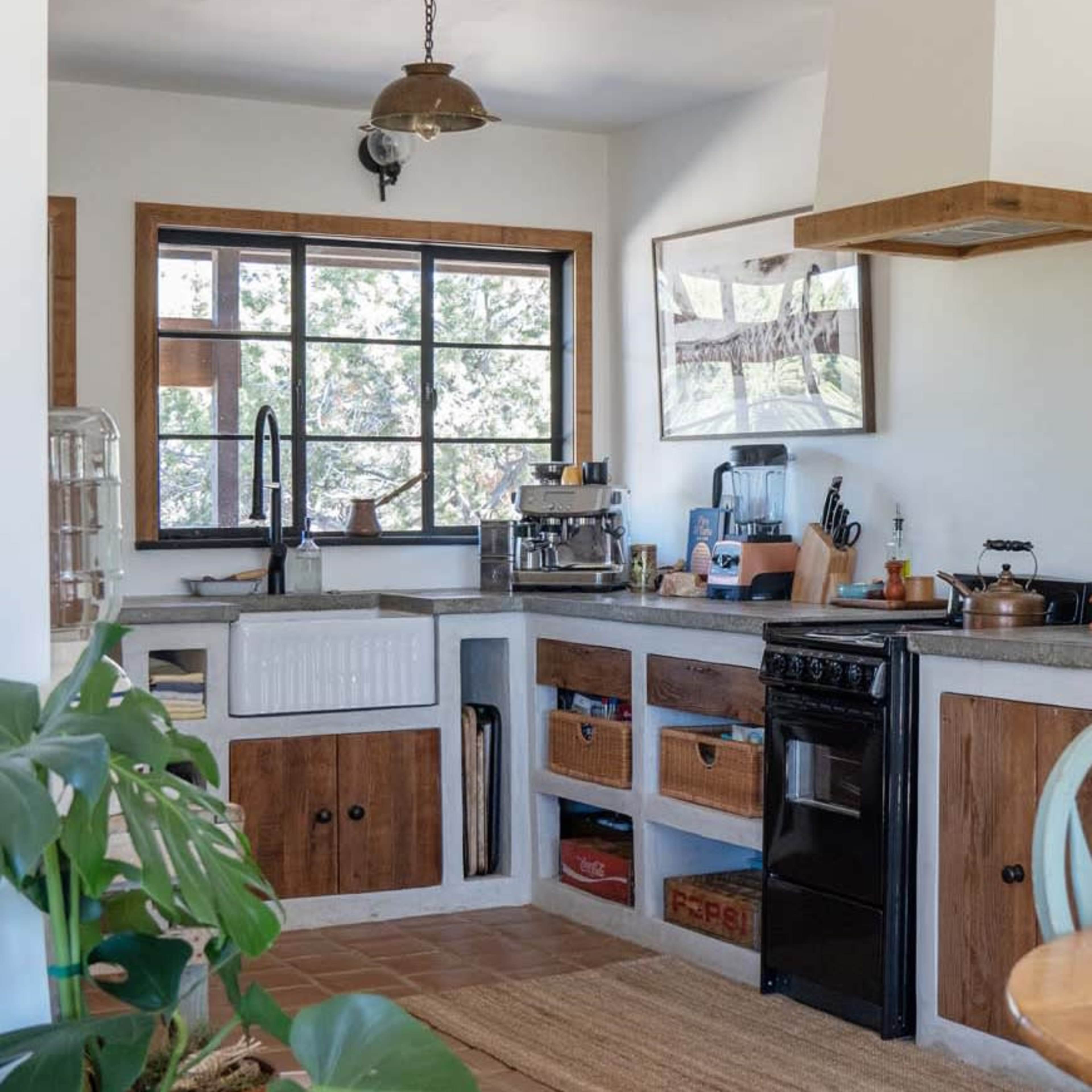 A kitchen features a black stove, sink with a wooden cabinet, and a large window overlooking greenery.