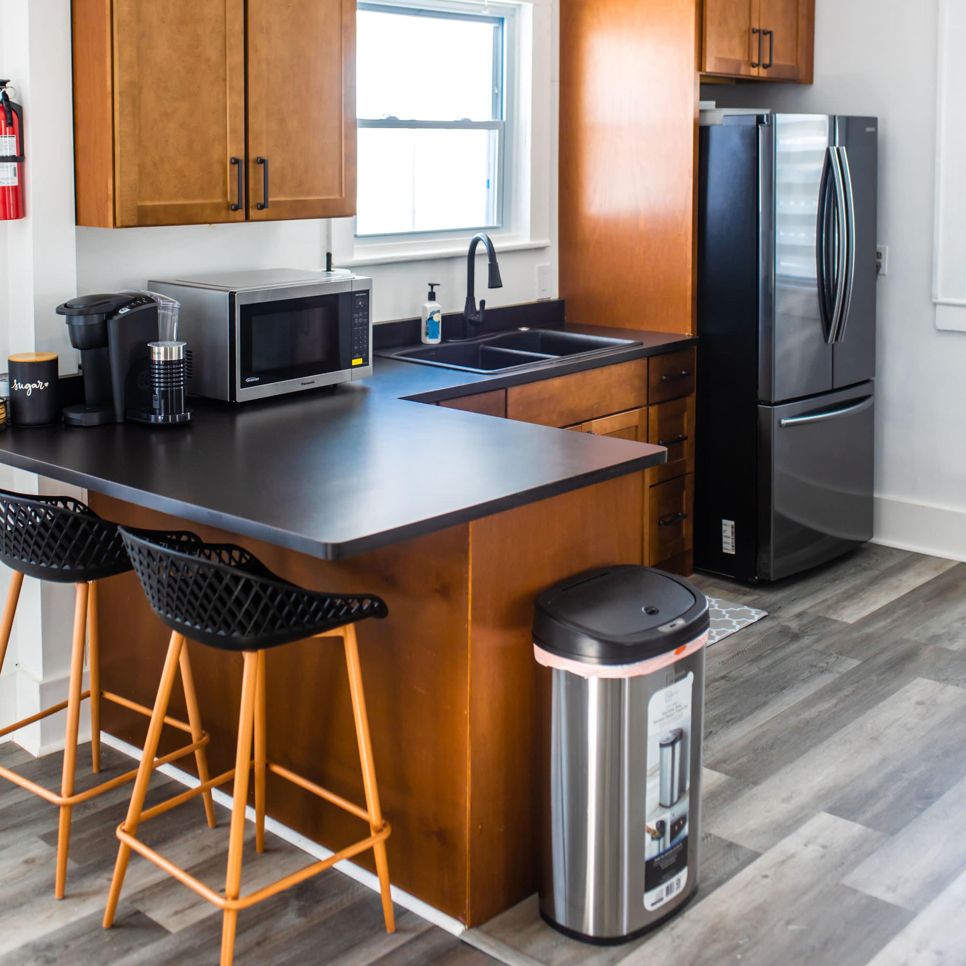 The kitchen features wooden cabinets, a black countertop with bar seating, modern appliances including a refrigerator and microwave, and a window providing natural light.