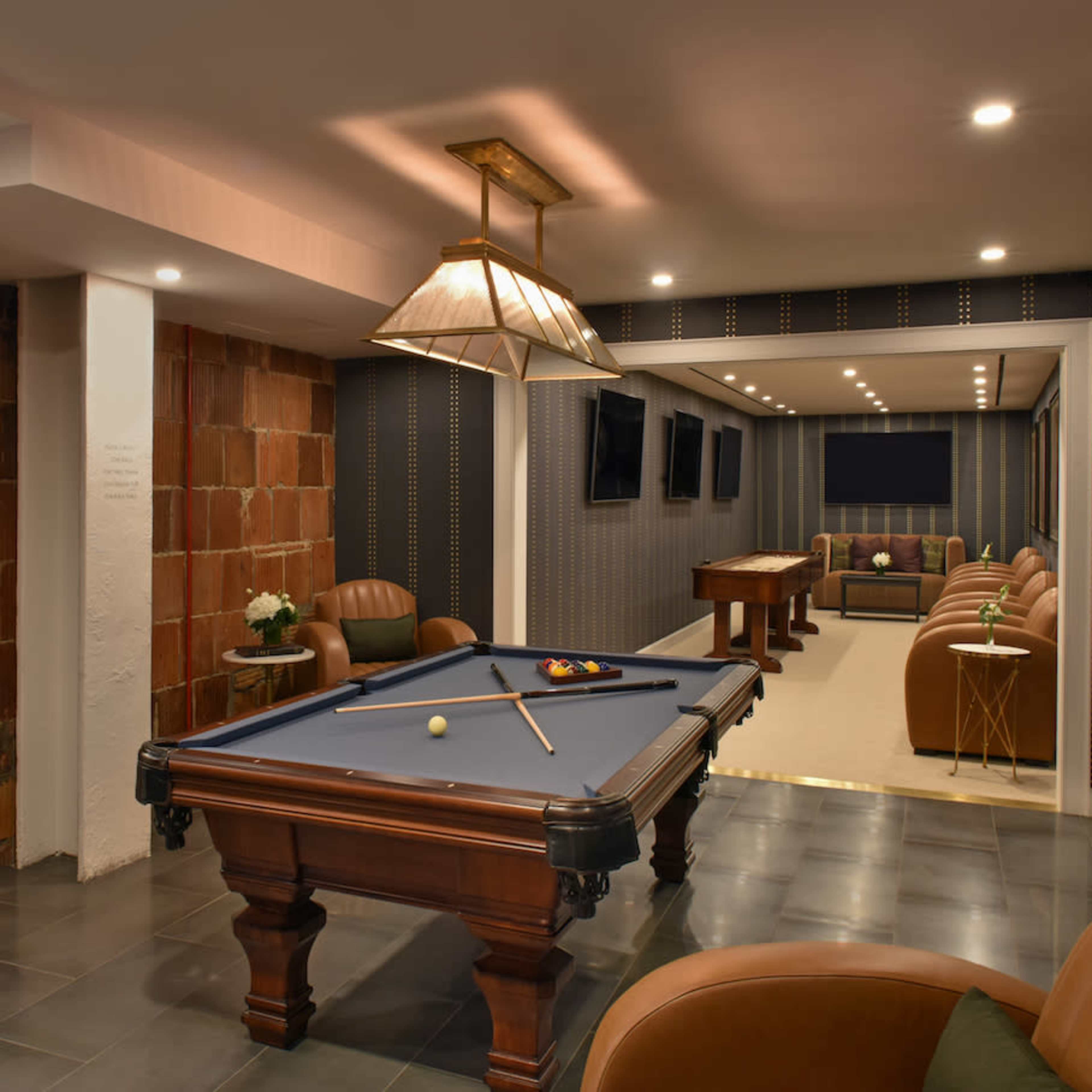 A modern game room featuring a billiard table, lounge seating, and multiple wall-mounted televisions.