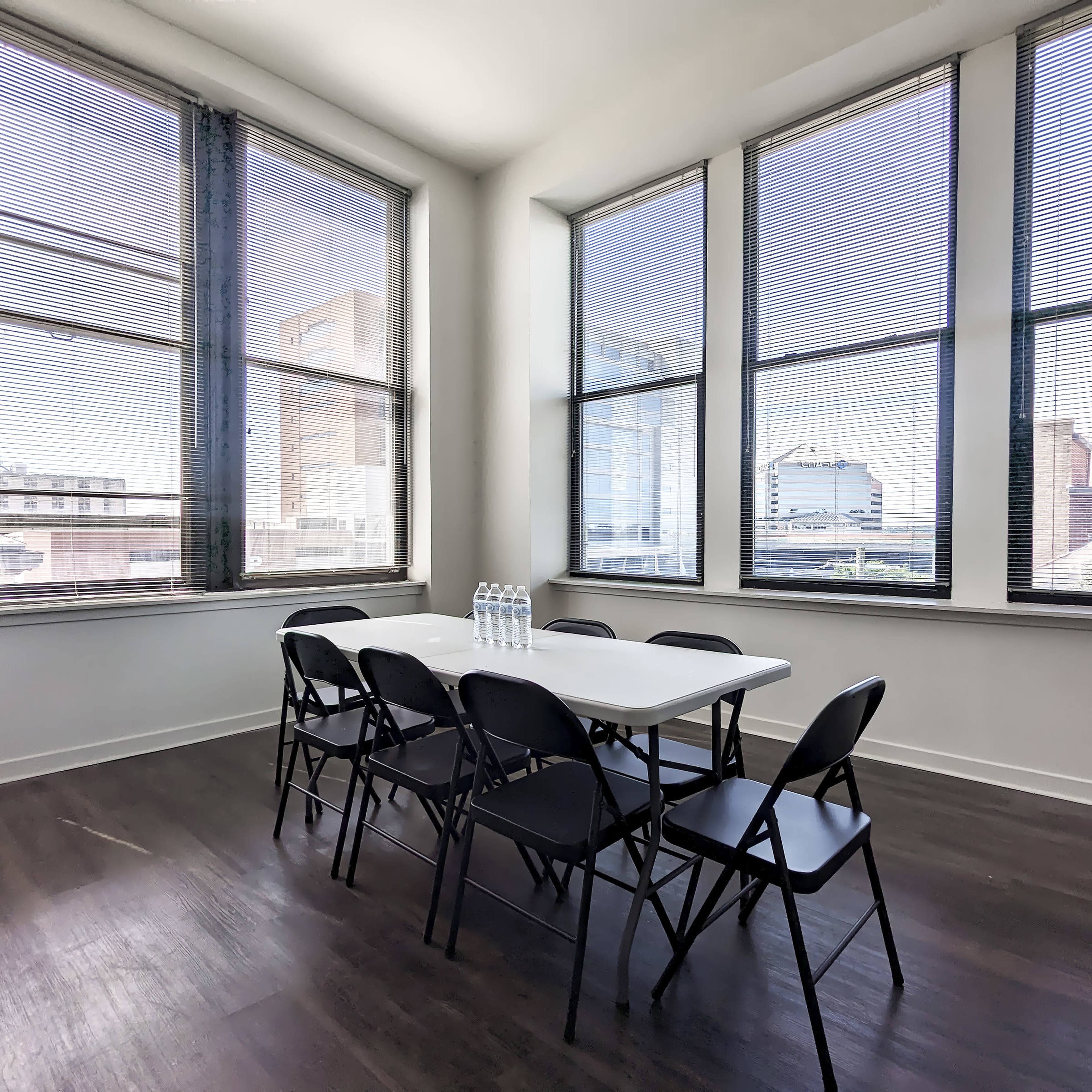 A conference room with a white table and six black chairs is illuminated by natural light from large windows.