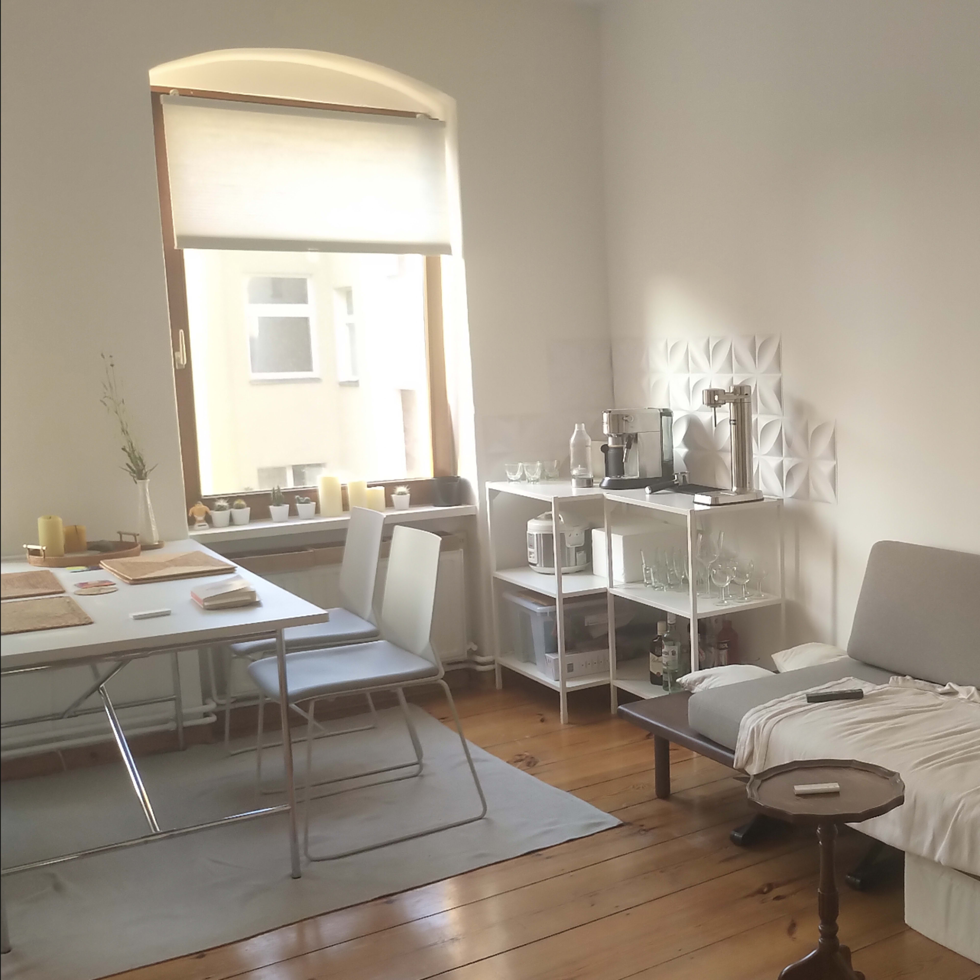 A living space features a gray sofa, a wooden table with chairs, and a window allowing natural light to enter.