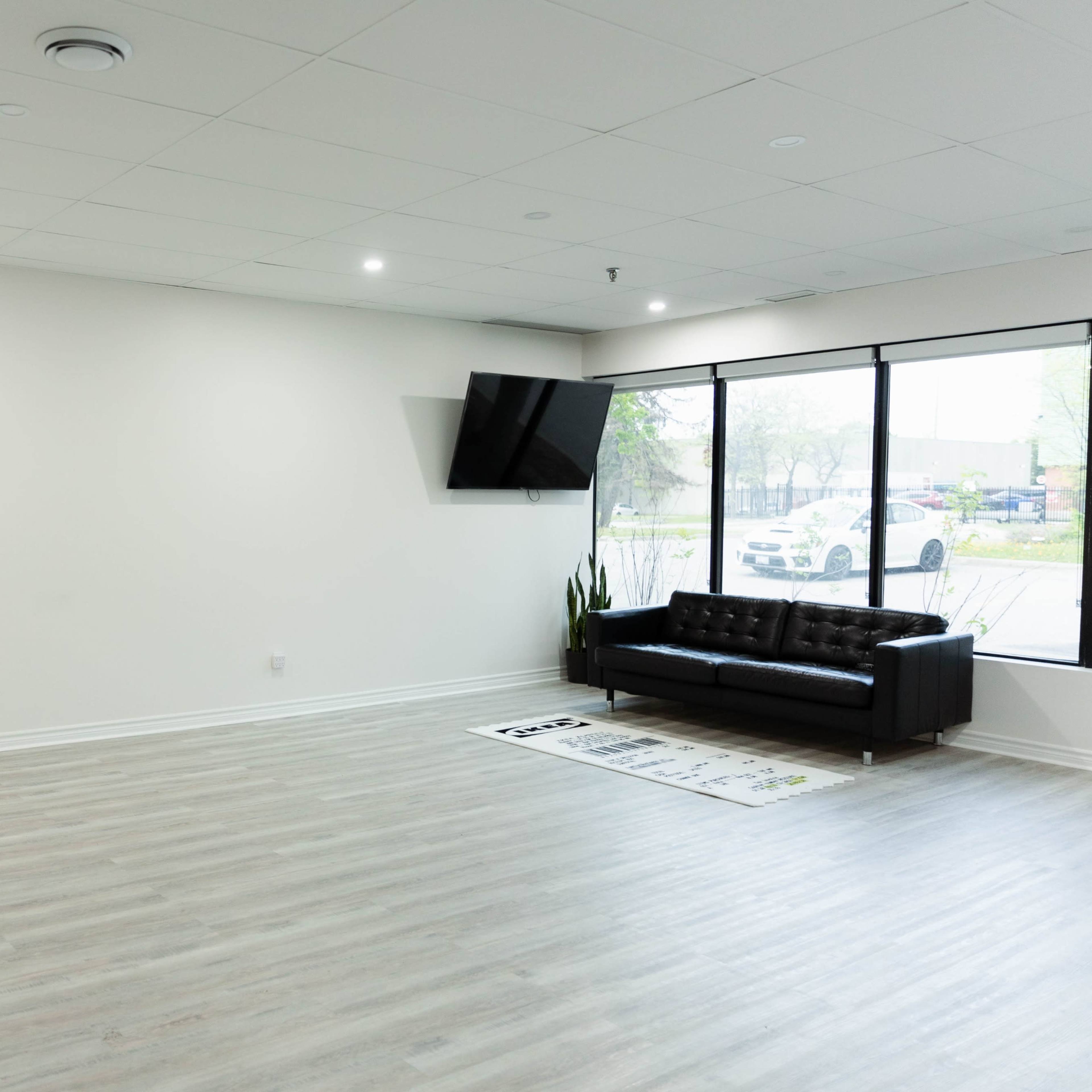 A spacious, empty room with a black couch, a large mirror, and a television mounted on the wall.