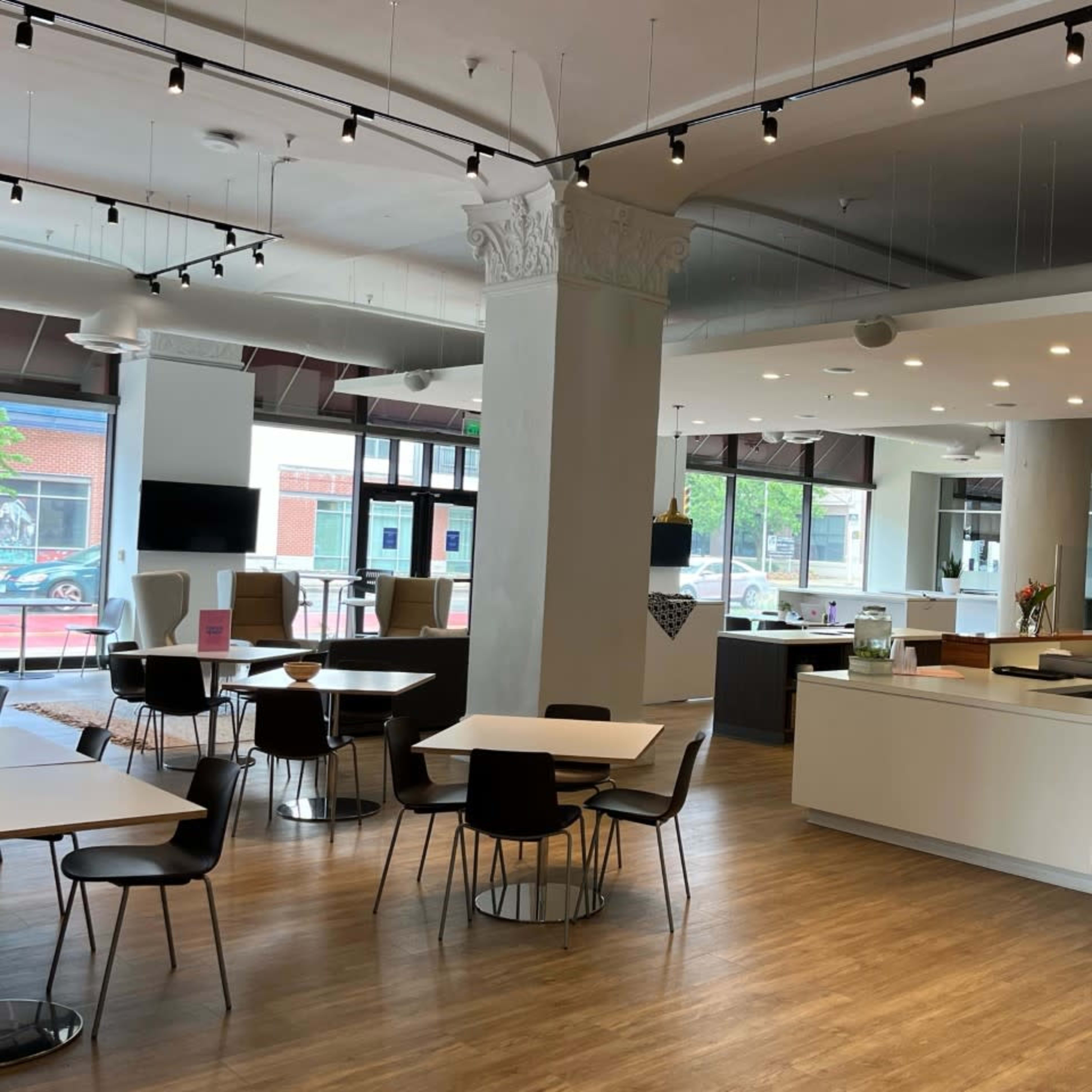 A modern, open interior space with dining tables, chairs, and a kitchenette area featuring stainless steel appliances.