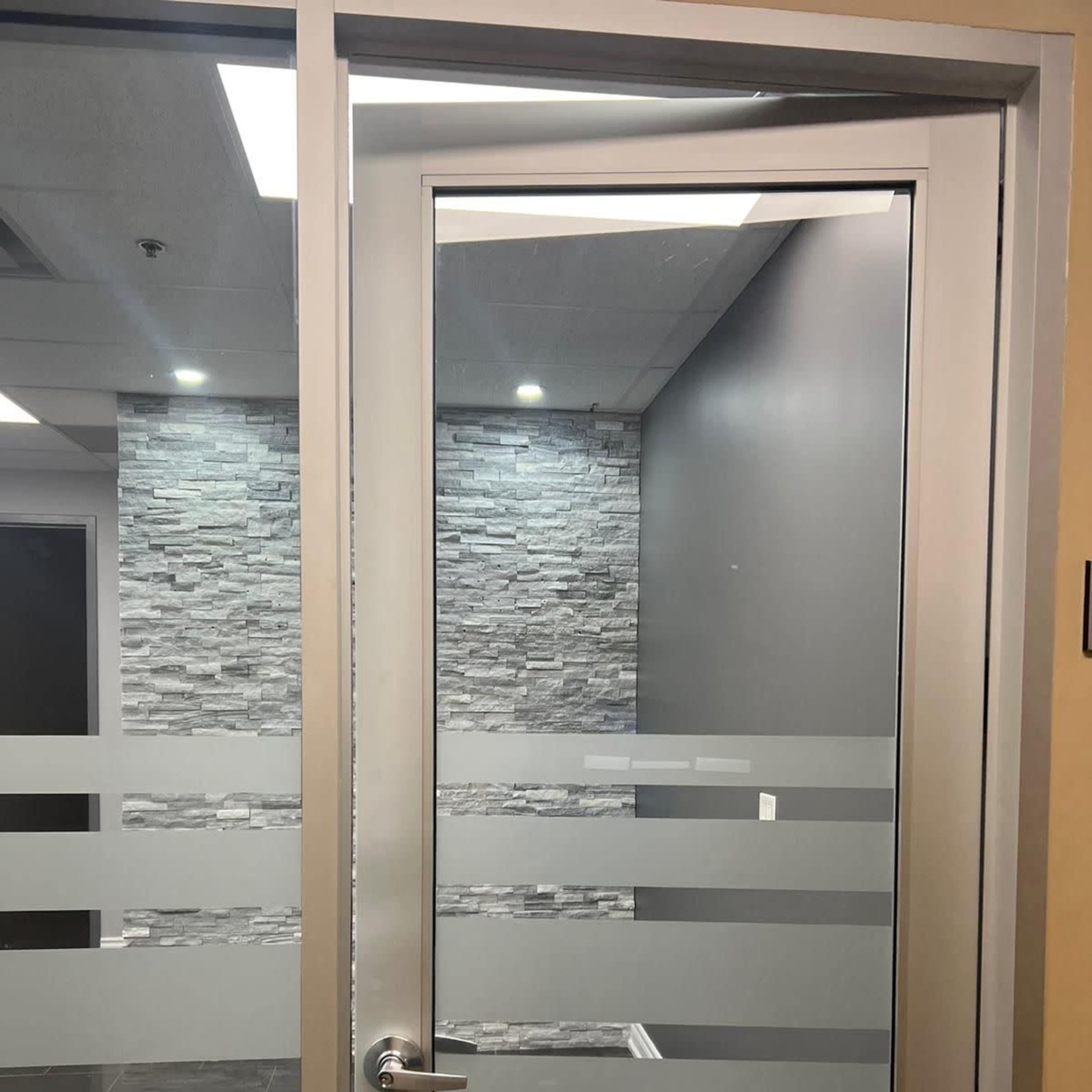 A glass door with horizontal frosted stripes, leading to a room with stone wall accents and neutral-colored walls.