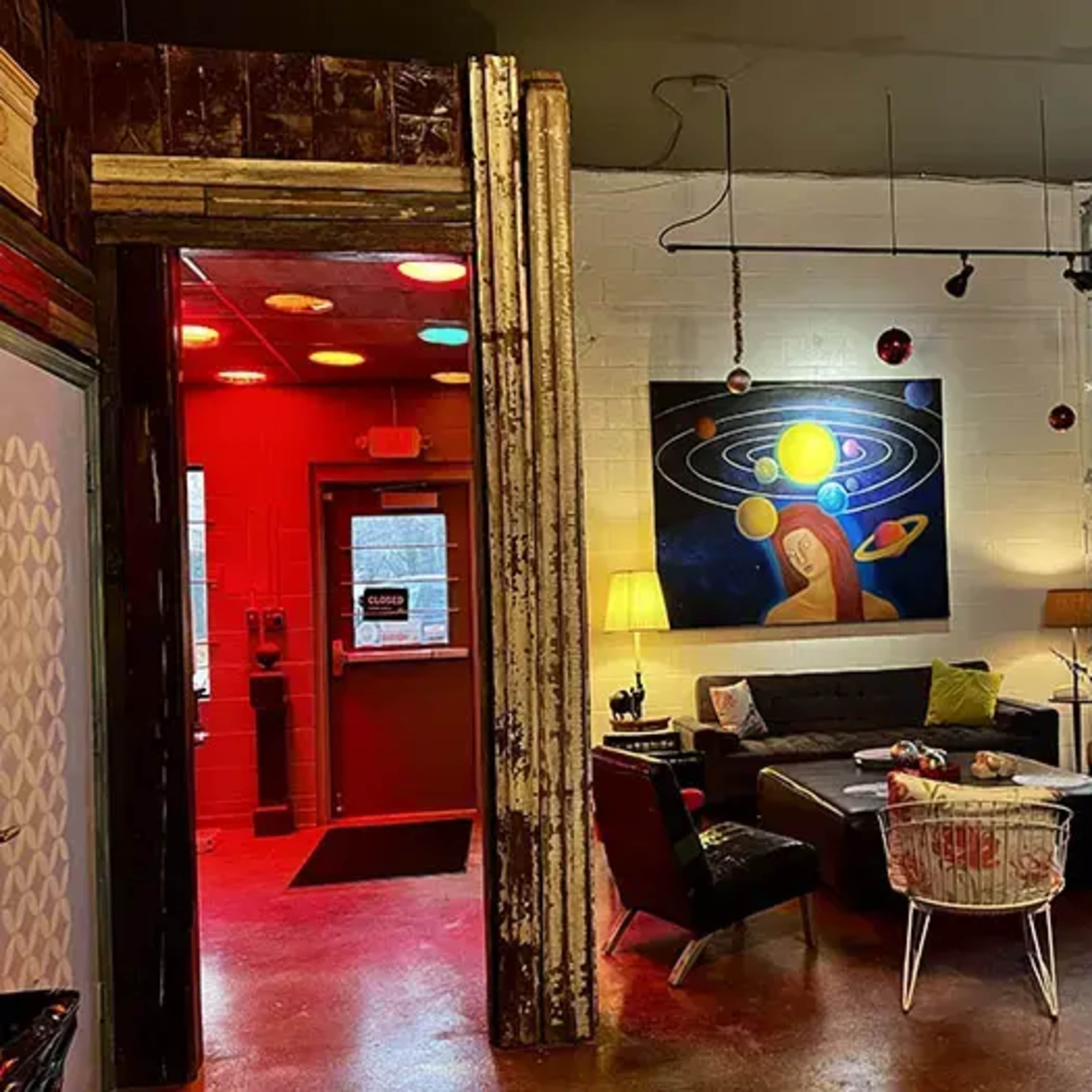 A modern, eclectic lounge area with a colorful painting of planets on the wall and a mix of comfortable furniture in a well-lit space.