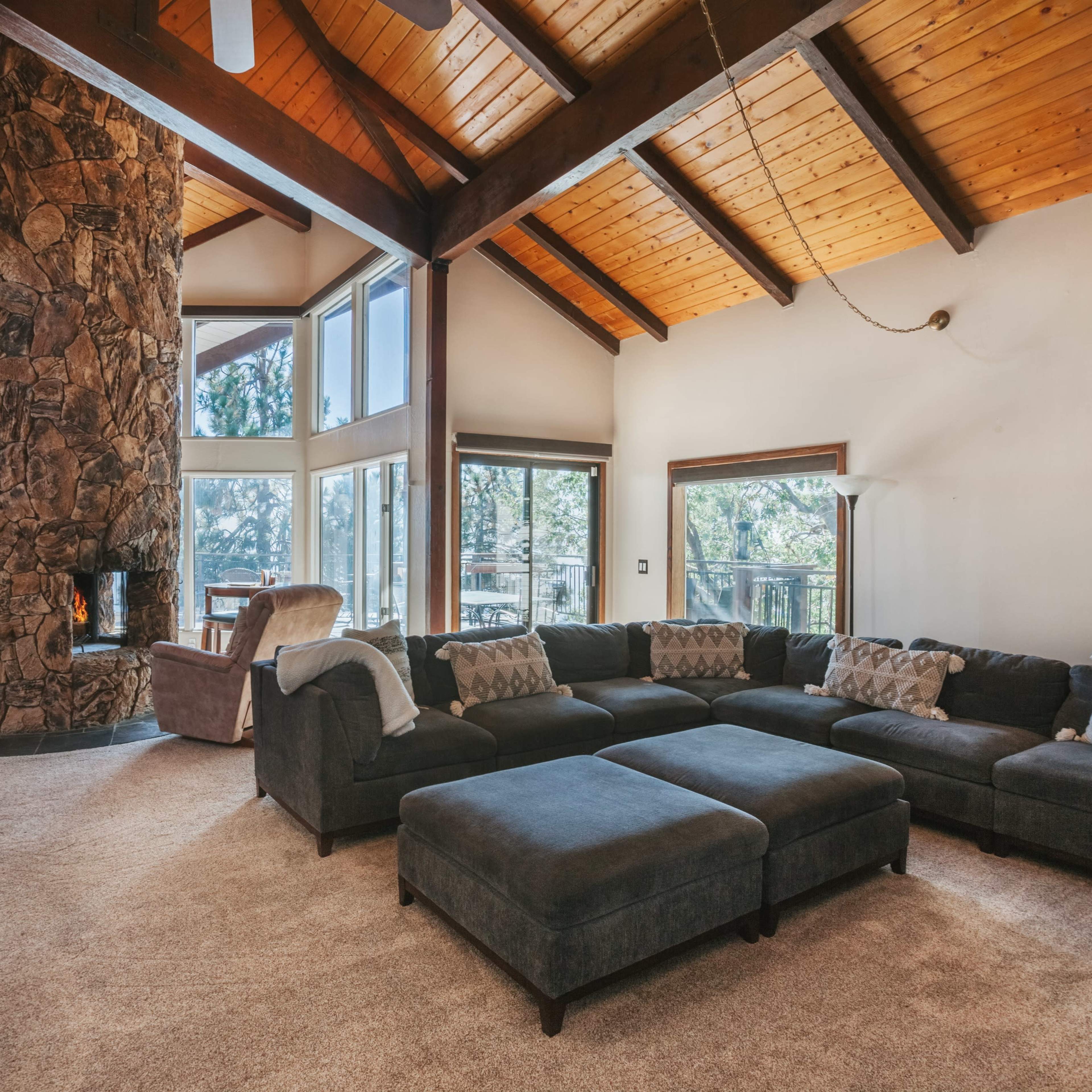 A spacious living room featuring a large sectional sofa, a stone fireplace, and high, wooden-beamed ceilings.