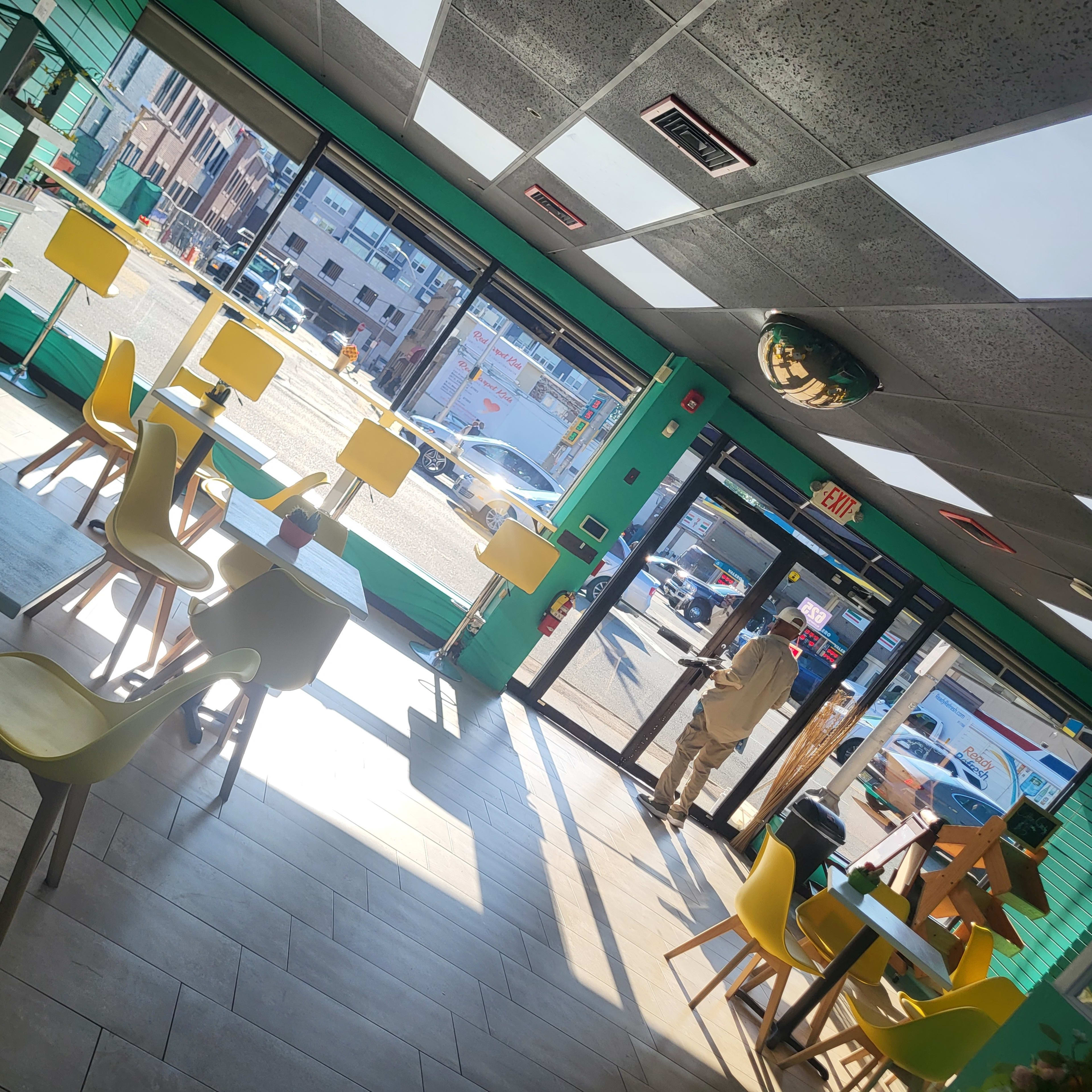 A brightly lit café interior with yellow chairs and tables, looking out through large windows onto a street scene.