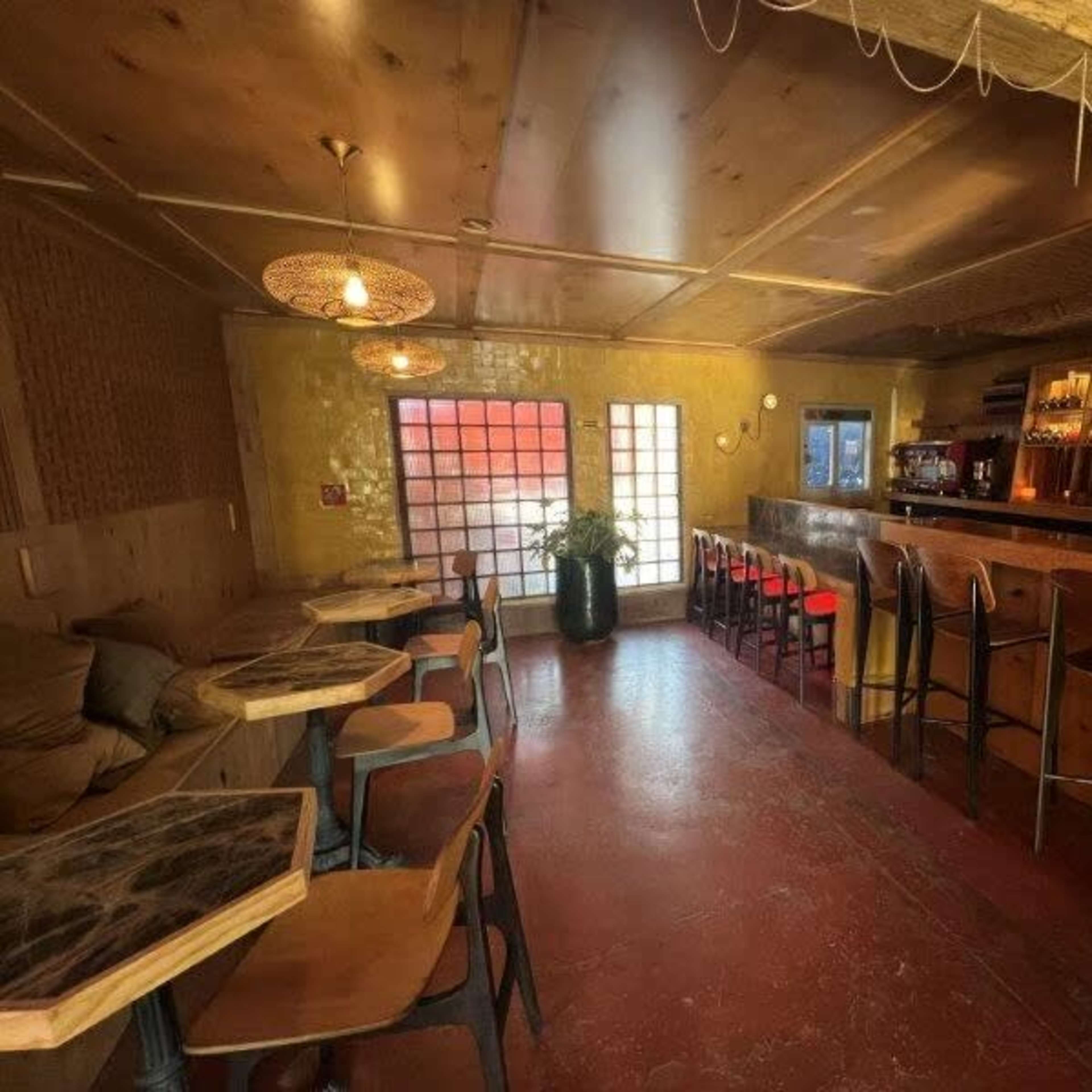 A cozy bar area with wooden furniture, a well-lit counter, and large windows letting in natural light.