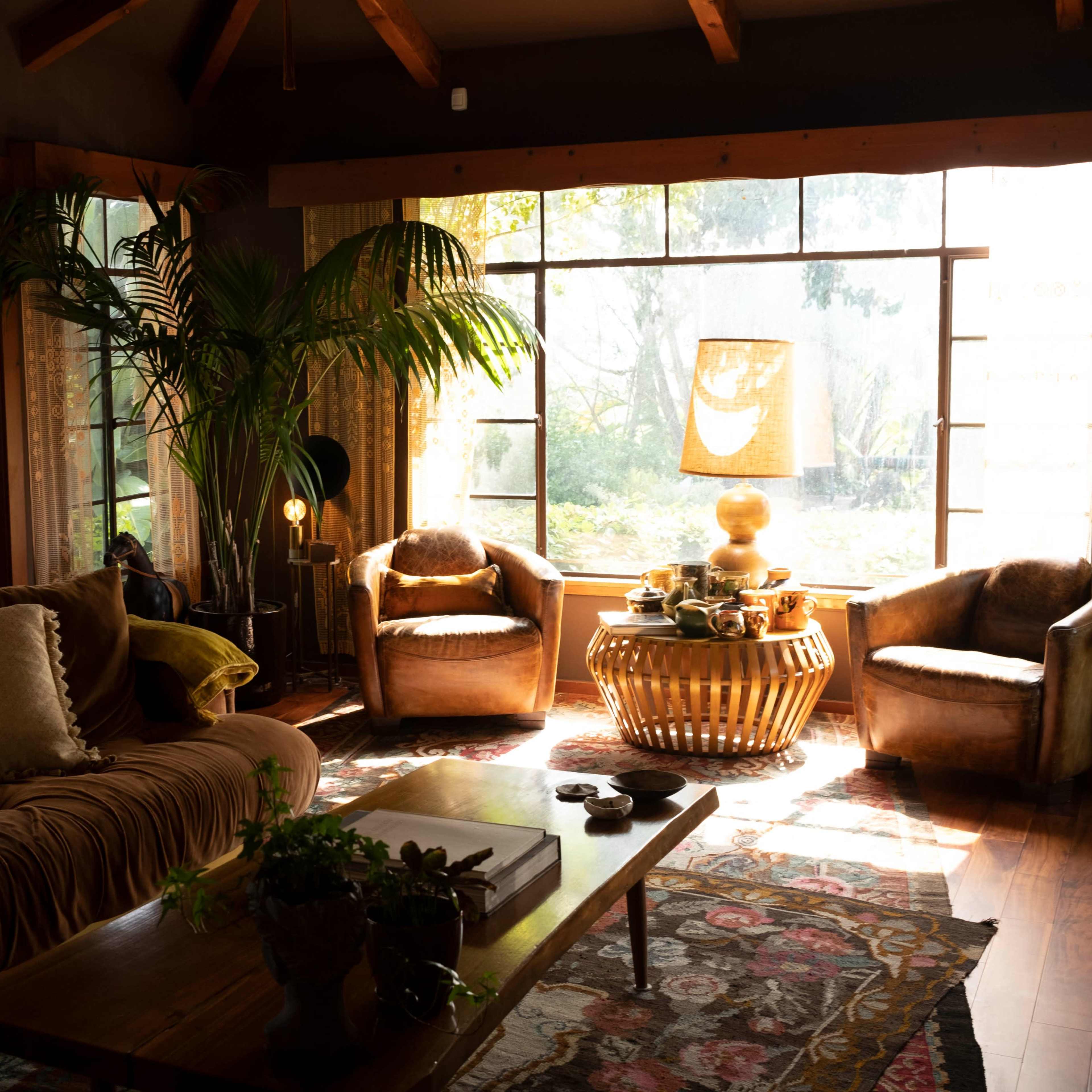 A cozy living room features a brown sofa, two upholstered chairs, a wooden coffee table, and large windows letting in natural light.