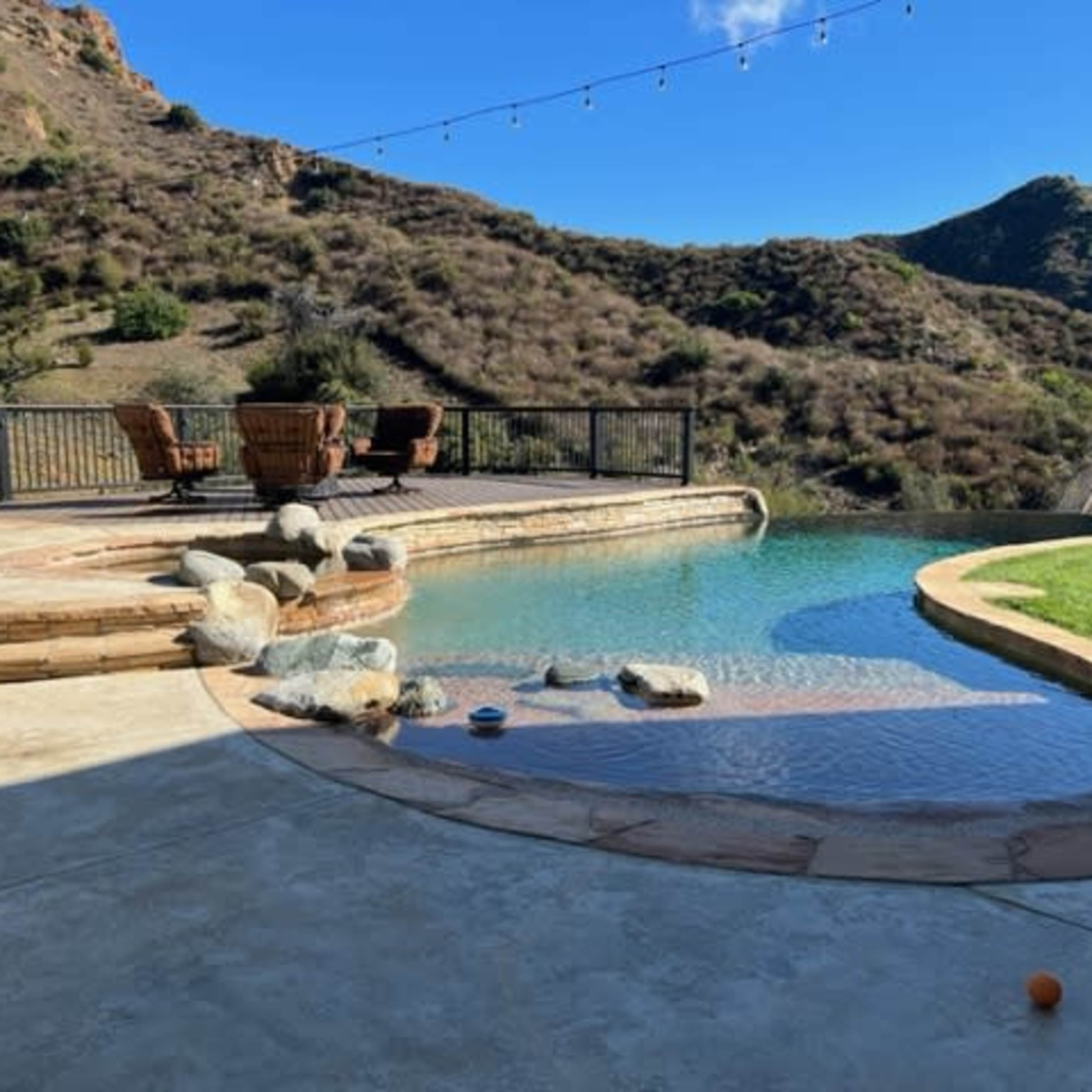 A backyard with a swimming pool, stone patio, and a view of rolling hills.