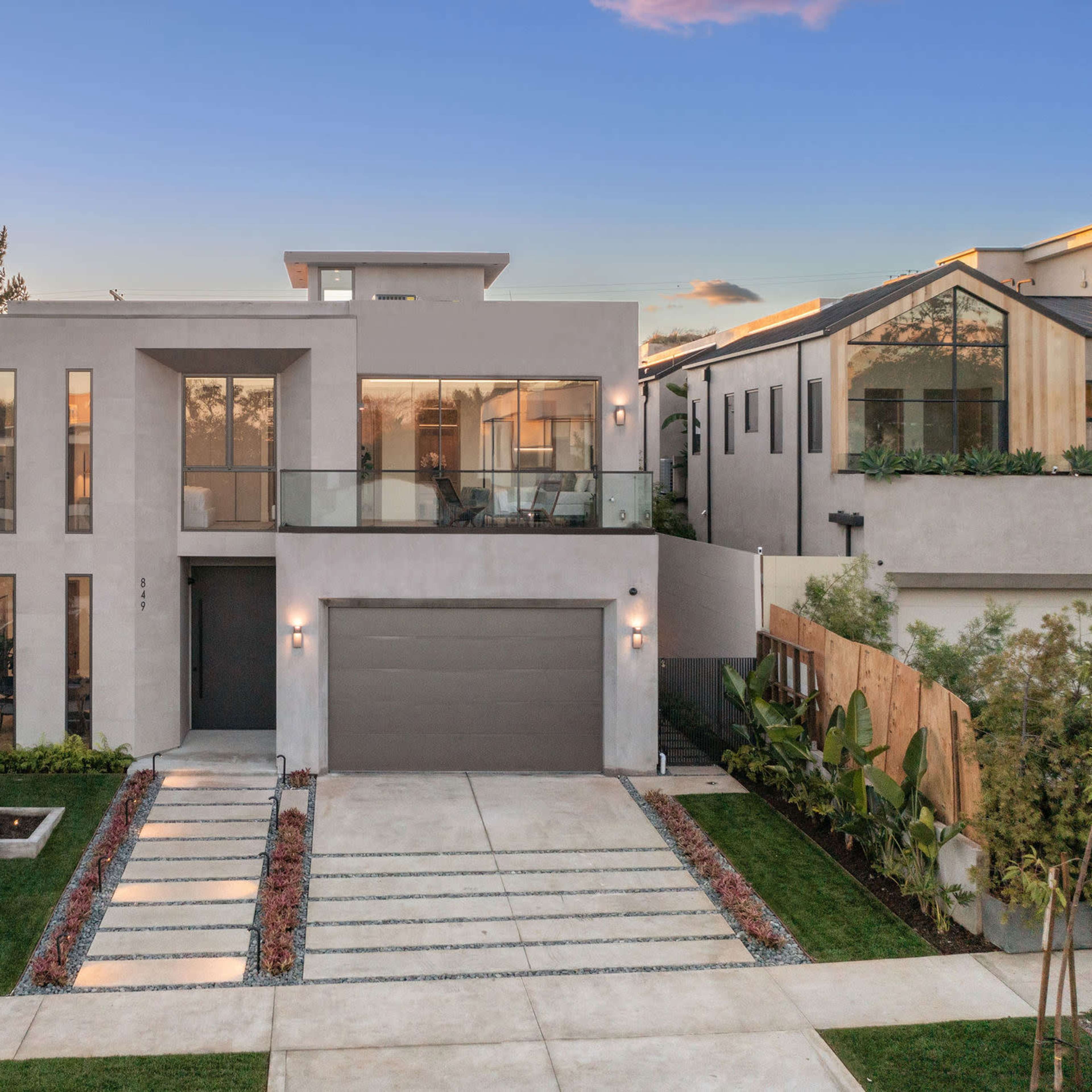 A modern two-story house with a garage, large windows, and a landscaped front yard featuring pathways and greenery.