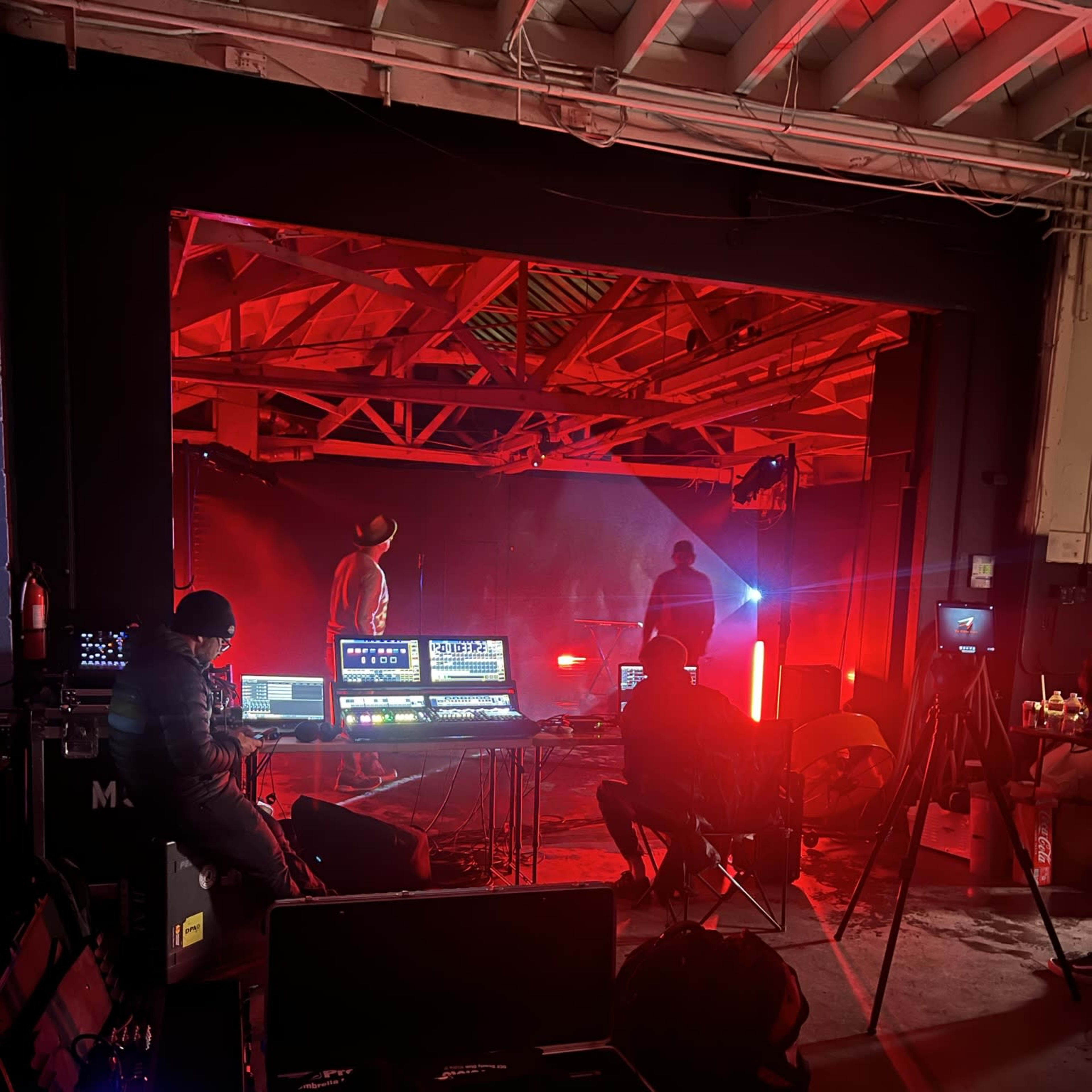 A group of technicians operates various equipment behind the scenes of a performance illuminated by red lights.