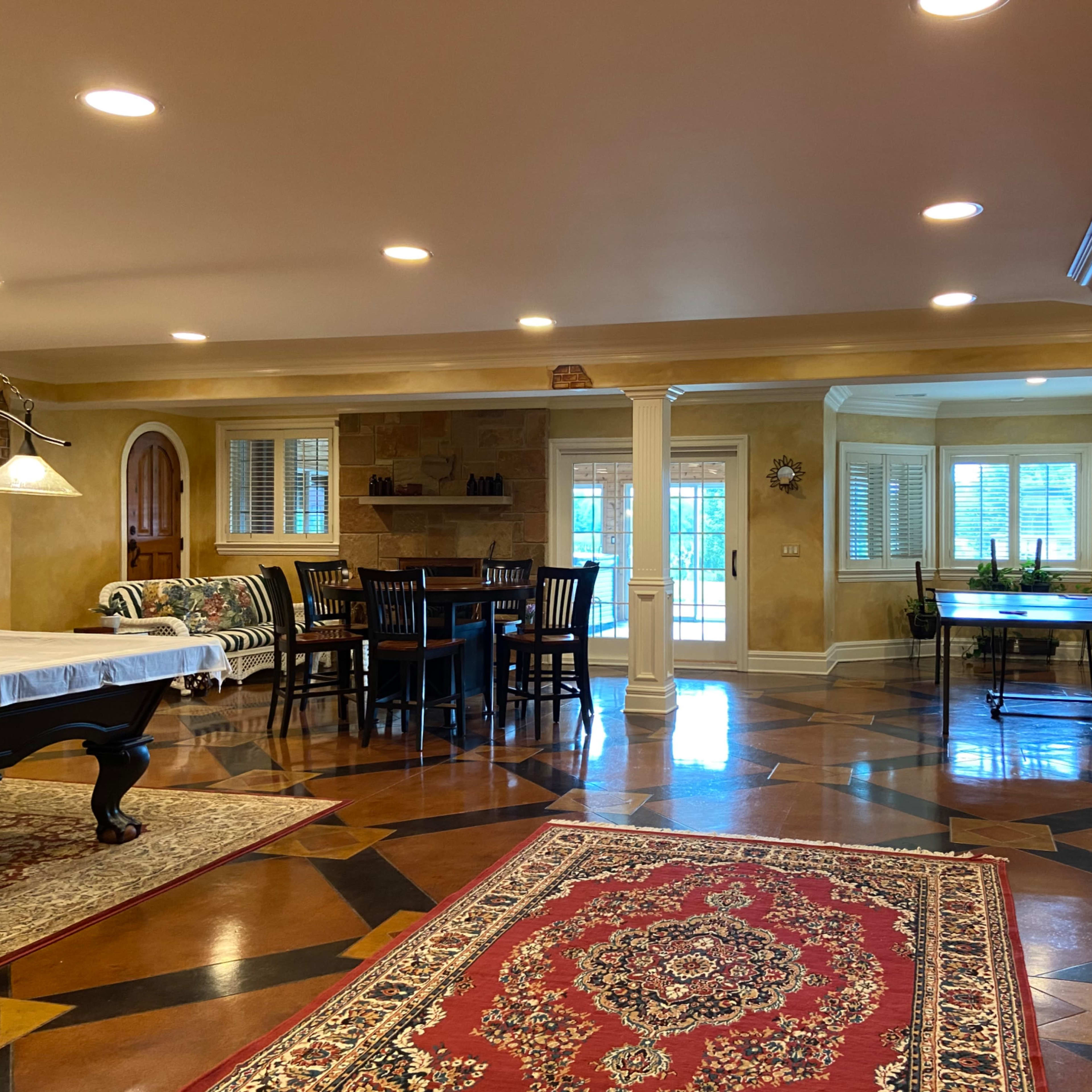 A spacious room with a dining area, a pool table covered with a white cloth, and wooden cabinetry along one wall.