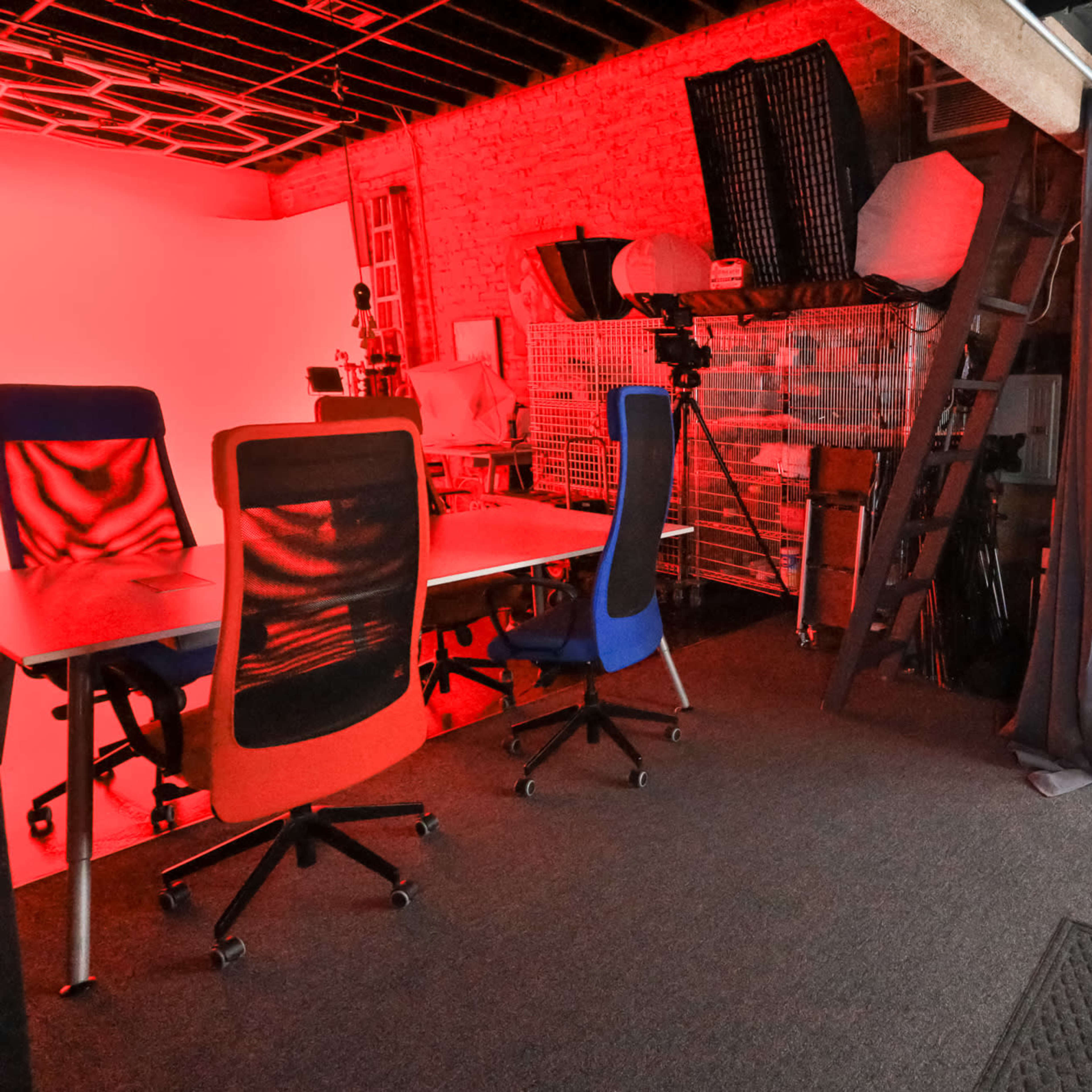 A workspace with two desks, one featuring red chairs, a ladder, and equipment, all set in a room with a red and gray color scheme.
