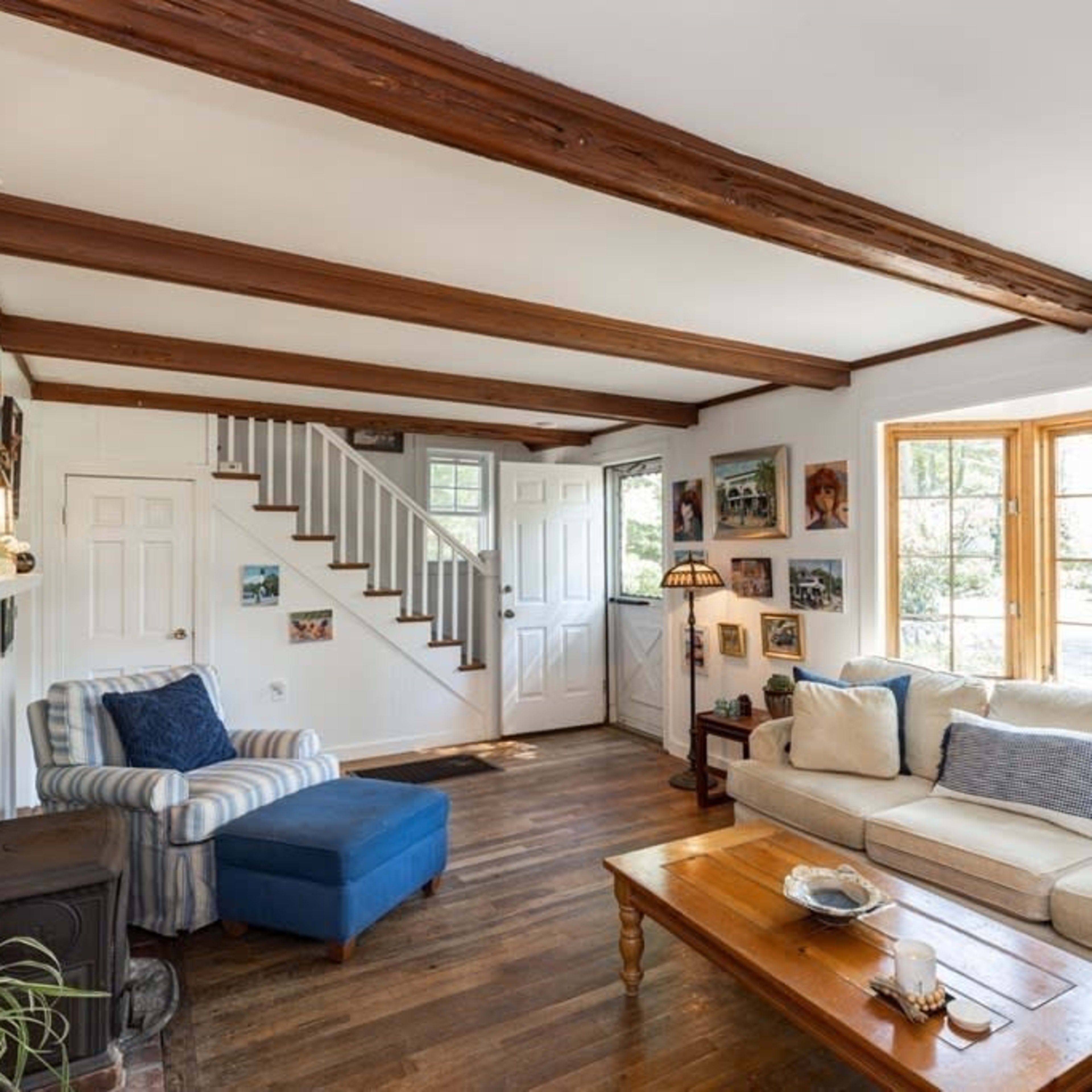 A cozy living room featuring a cream-colored sofa, a wooden coffee table, a blue armchair, and artwork displayed on the walls.