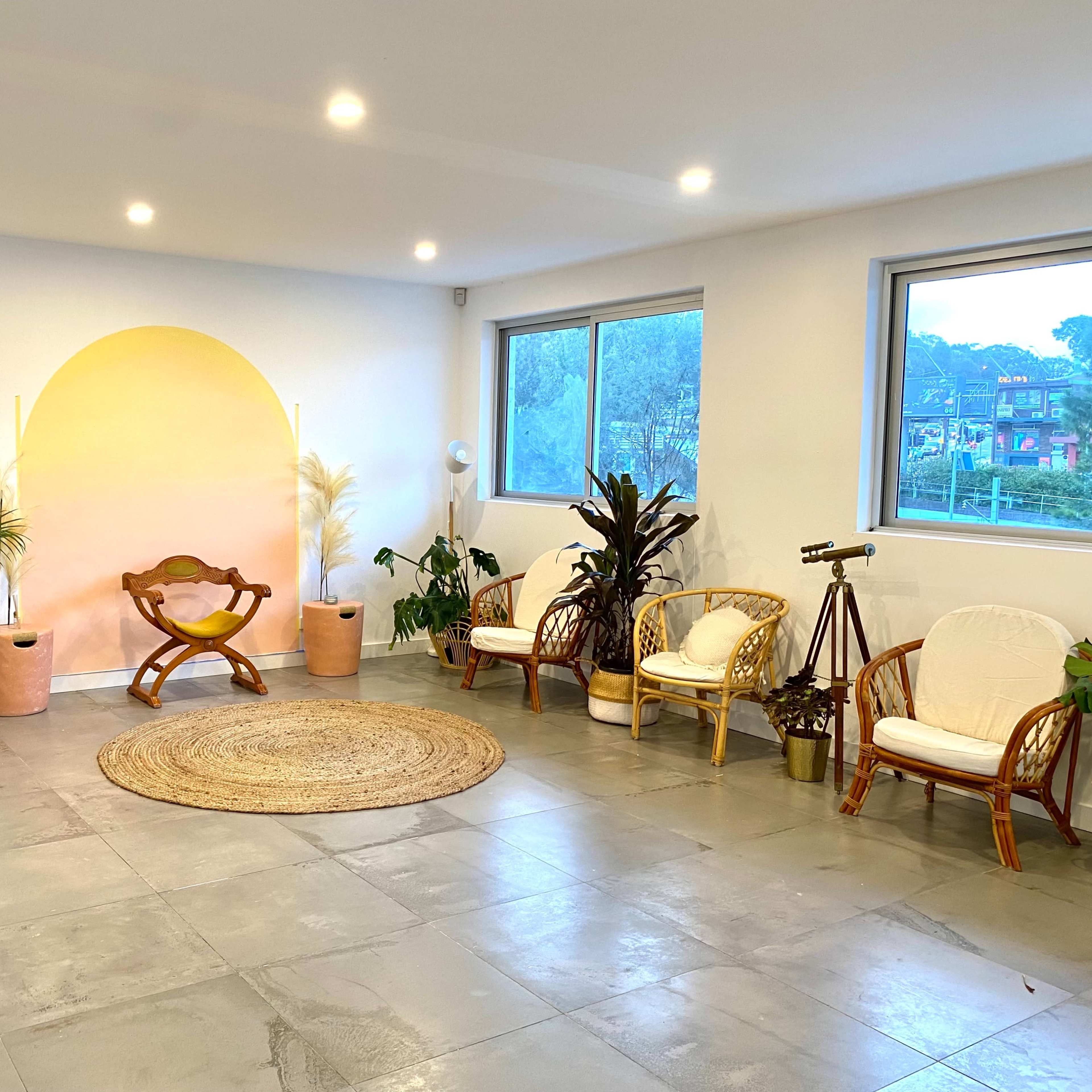 A spacious room features a light-colored wall with a circular mural, surrounded by various plants and seating arrangements.