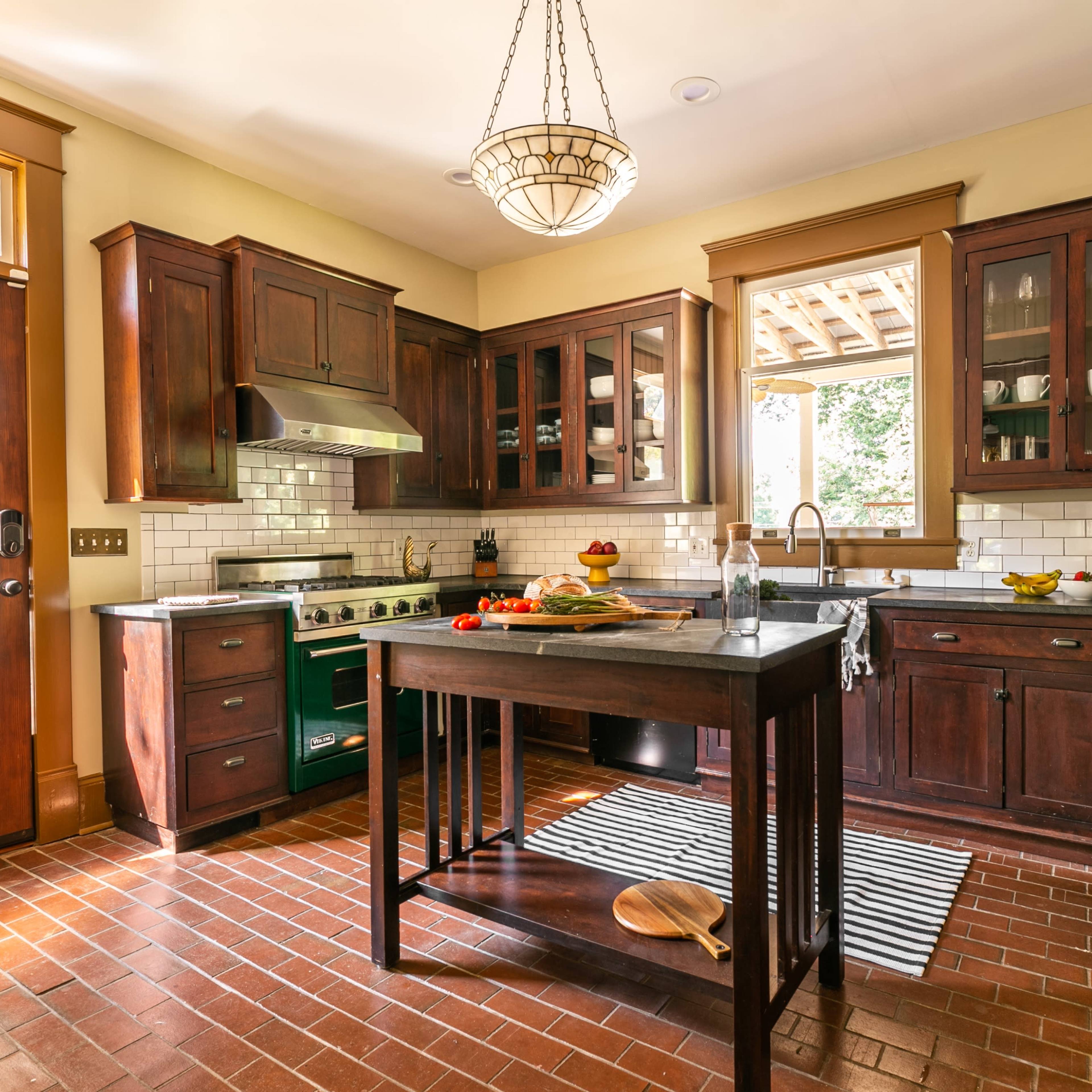 The kitchen features dark wood cabinets, a stainless steel refrigerator, and a central island with a marble countertop, illuminated by a hanging chandelier.