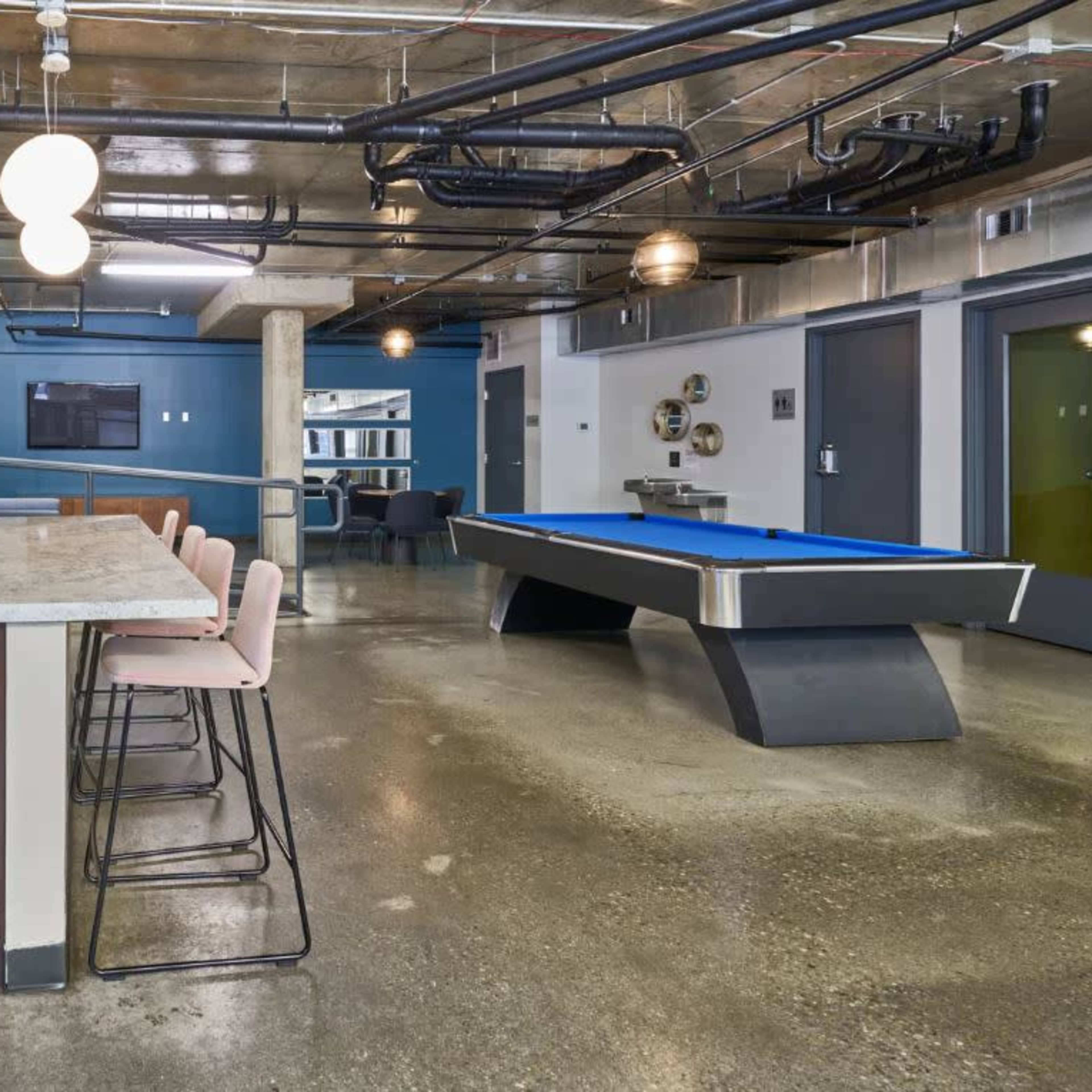 A modern open-concept kitchen and recreational area featuring a kitchen island with seating, a pool table, and industrial-style decor.
