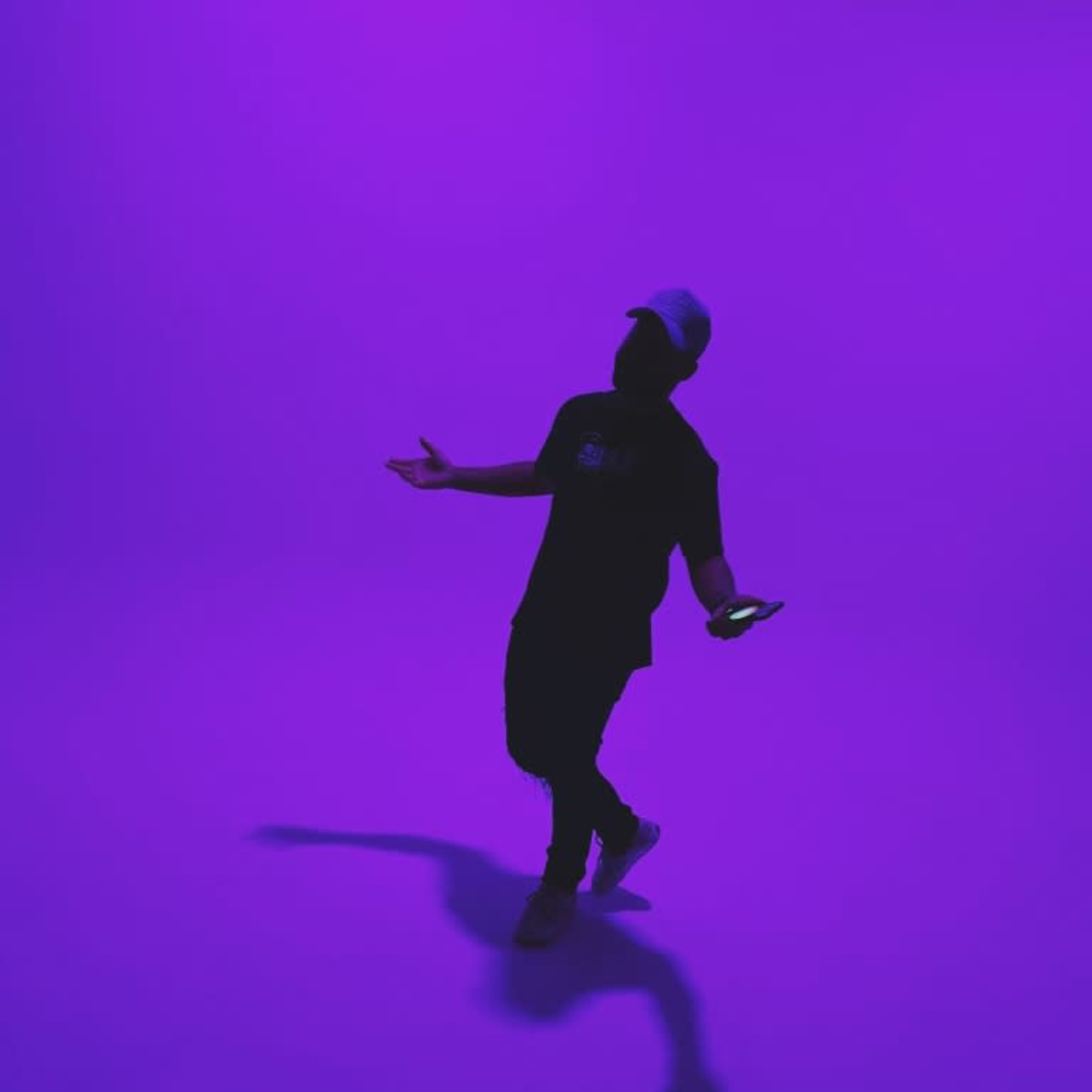 A person stands under a purple background while holding a phone and gesturing with their hands.