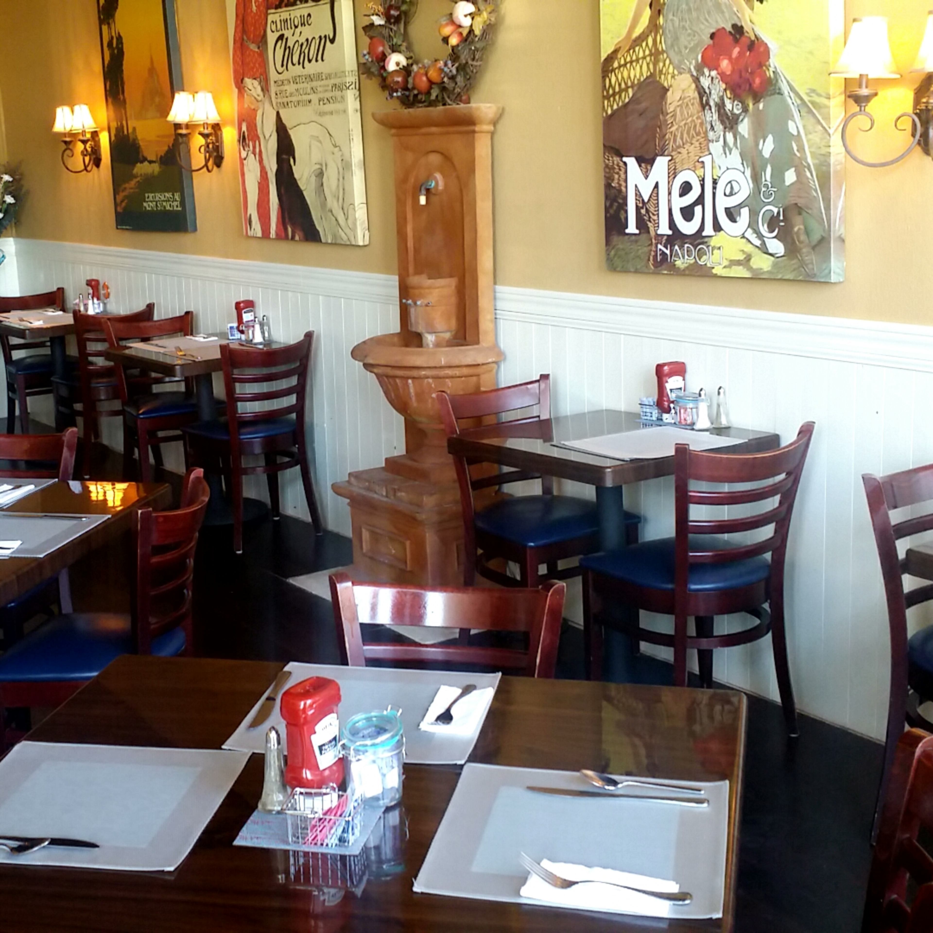 A restaurant interior with wooden tables and chairs, decorated walls featuring vintage posters, and a small fountain in the corner.