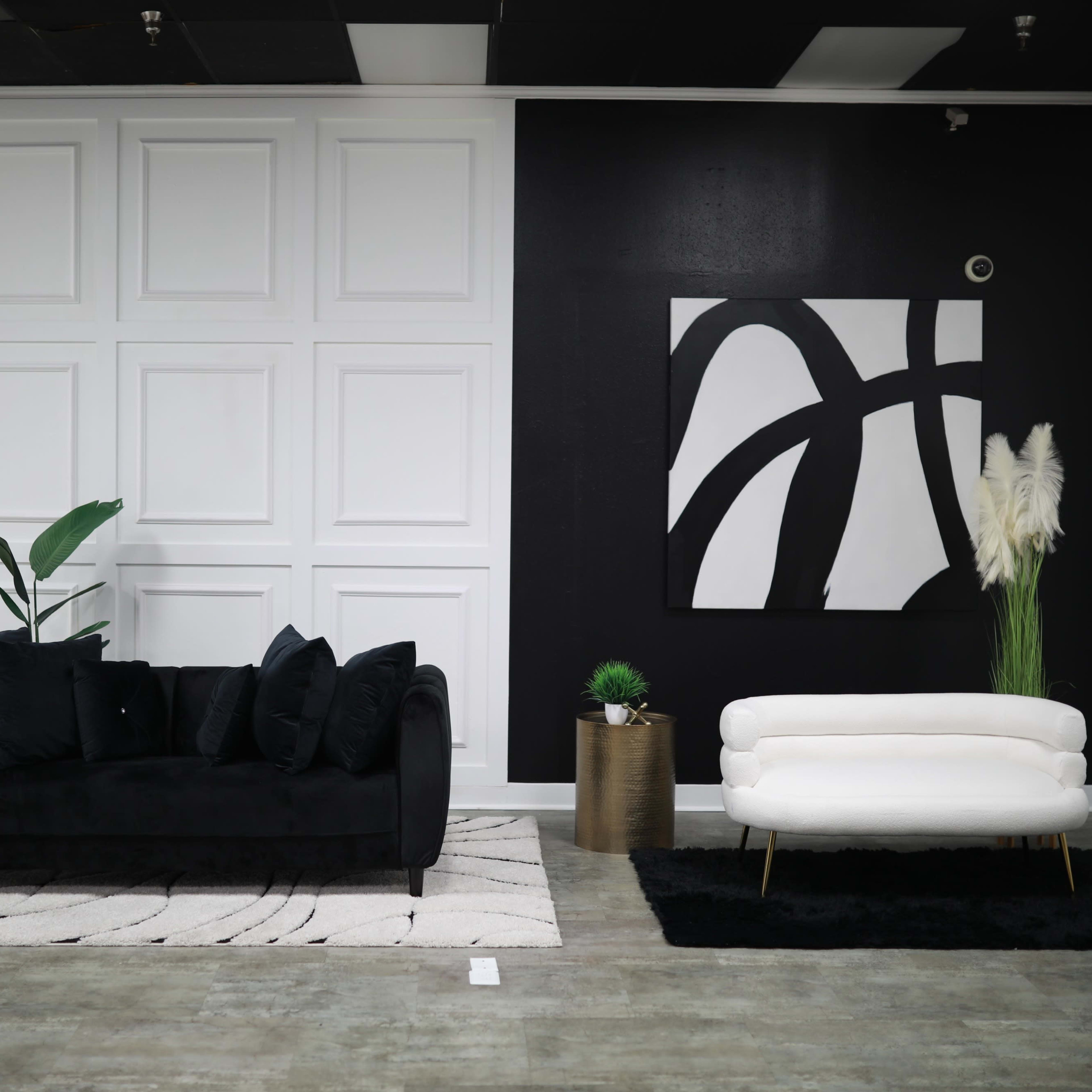 A modern interior with a black sofa and a white loveseat, arranged on a patterned rug against a backdrop of white and black walls.