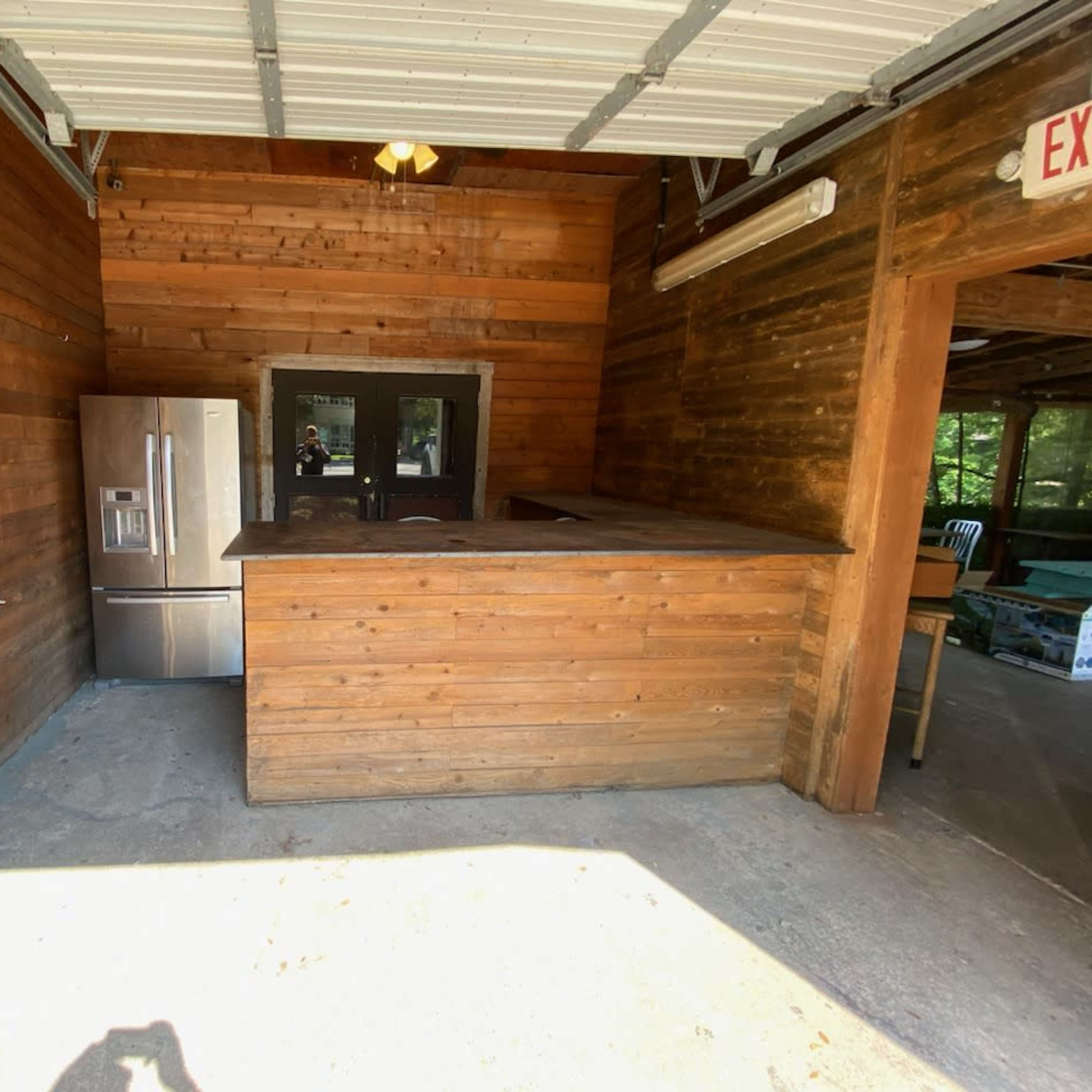 A wooden interior with a large counter and a stainless steel refrigerator against the wall.