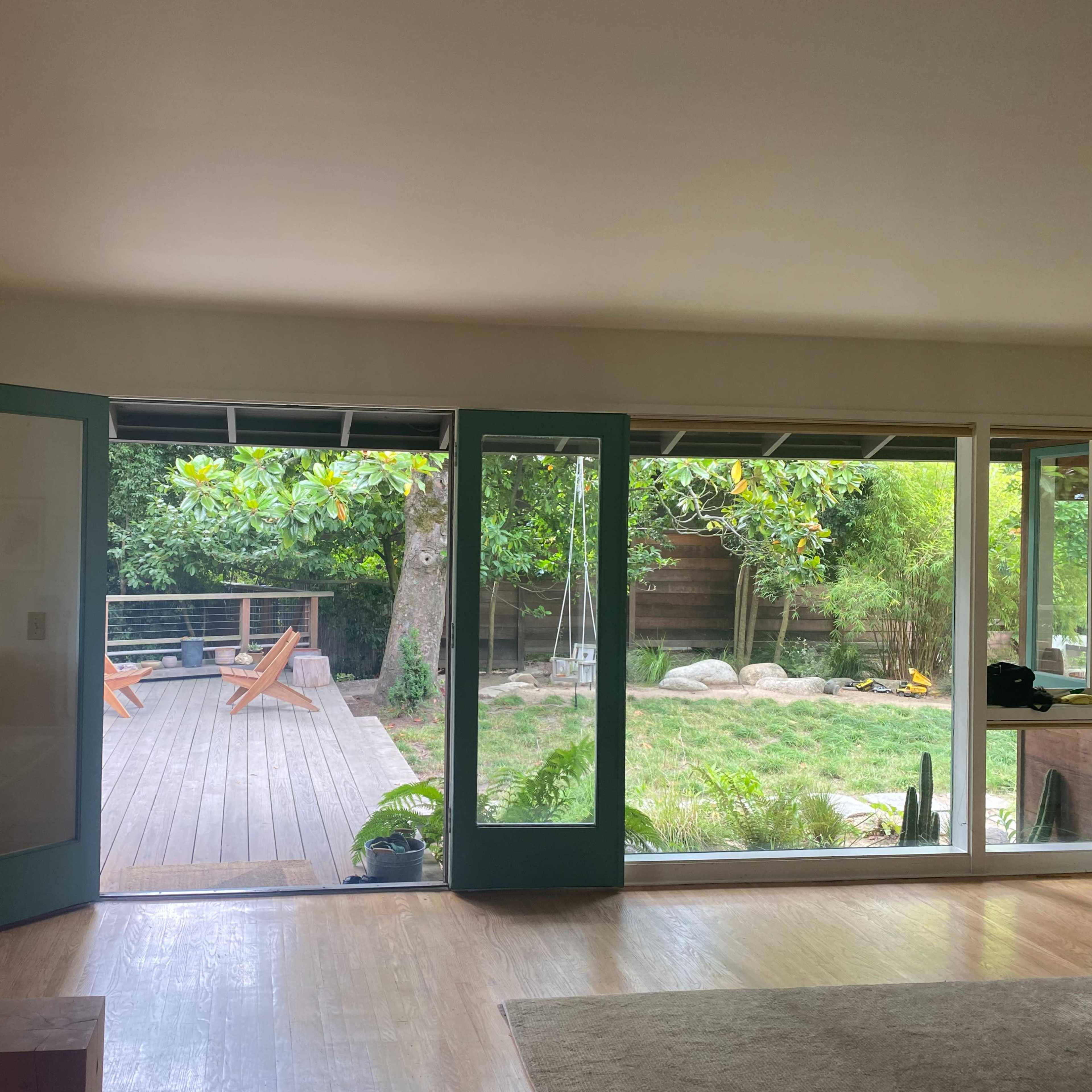 An interior room with large glass doors opening to a wooden deck surrounded by greenery.