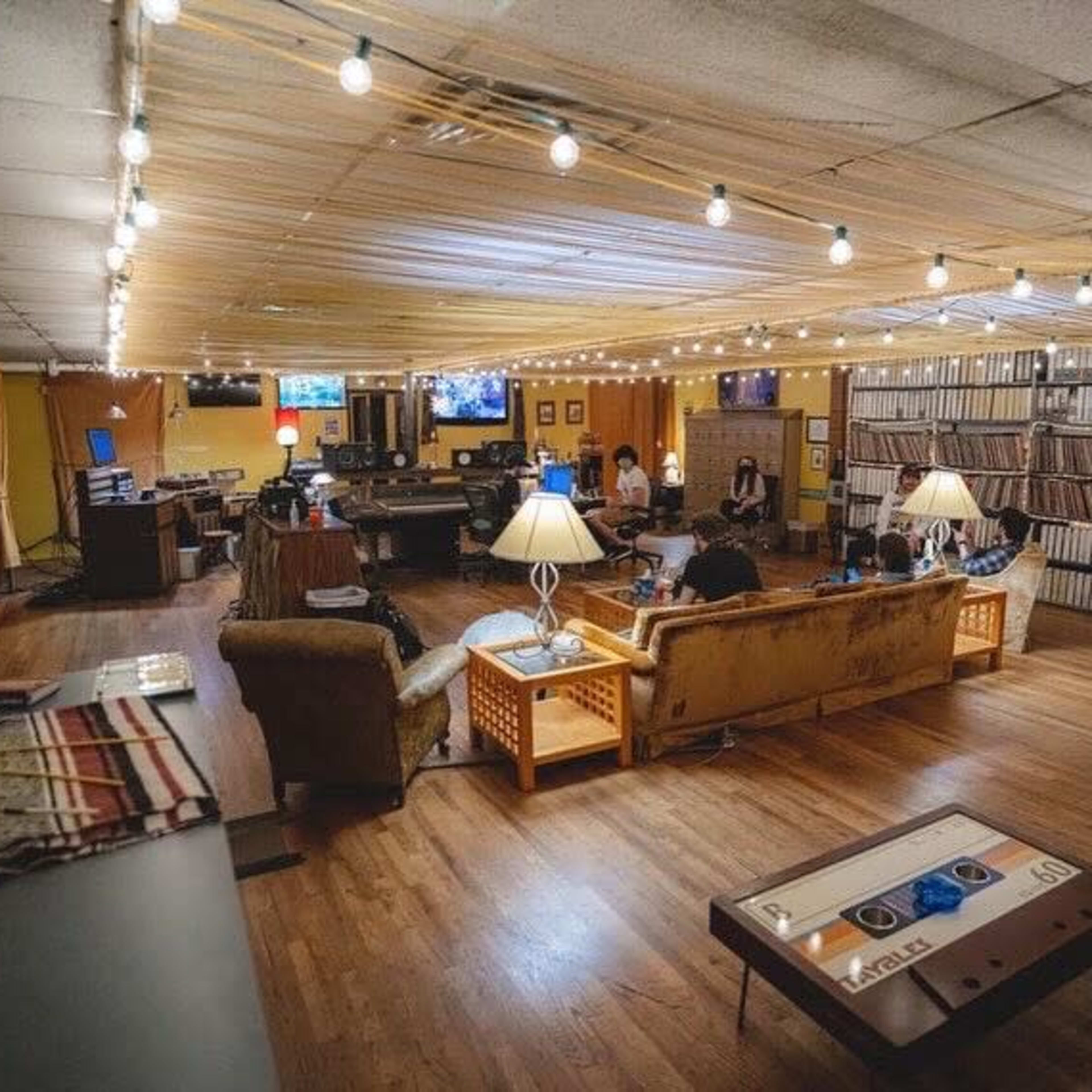 A spacious, well-lit lounge area with several couches, tables, and screens, where people are seated and engaging in various activities.