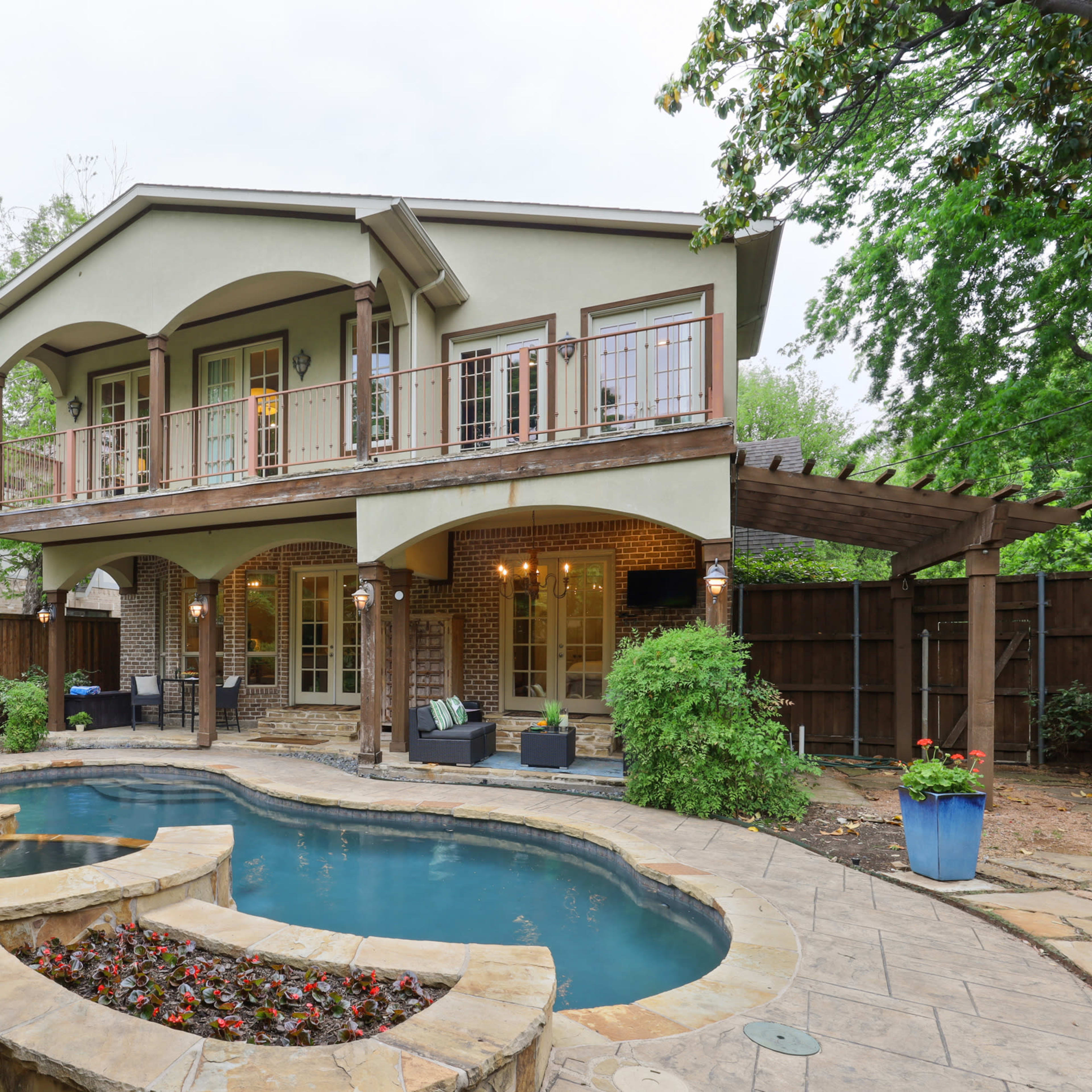 A two-story house with a backyard that features a curved swimming pool, stone patio, and a small garden area.