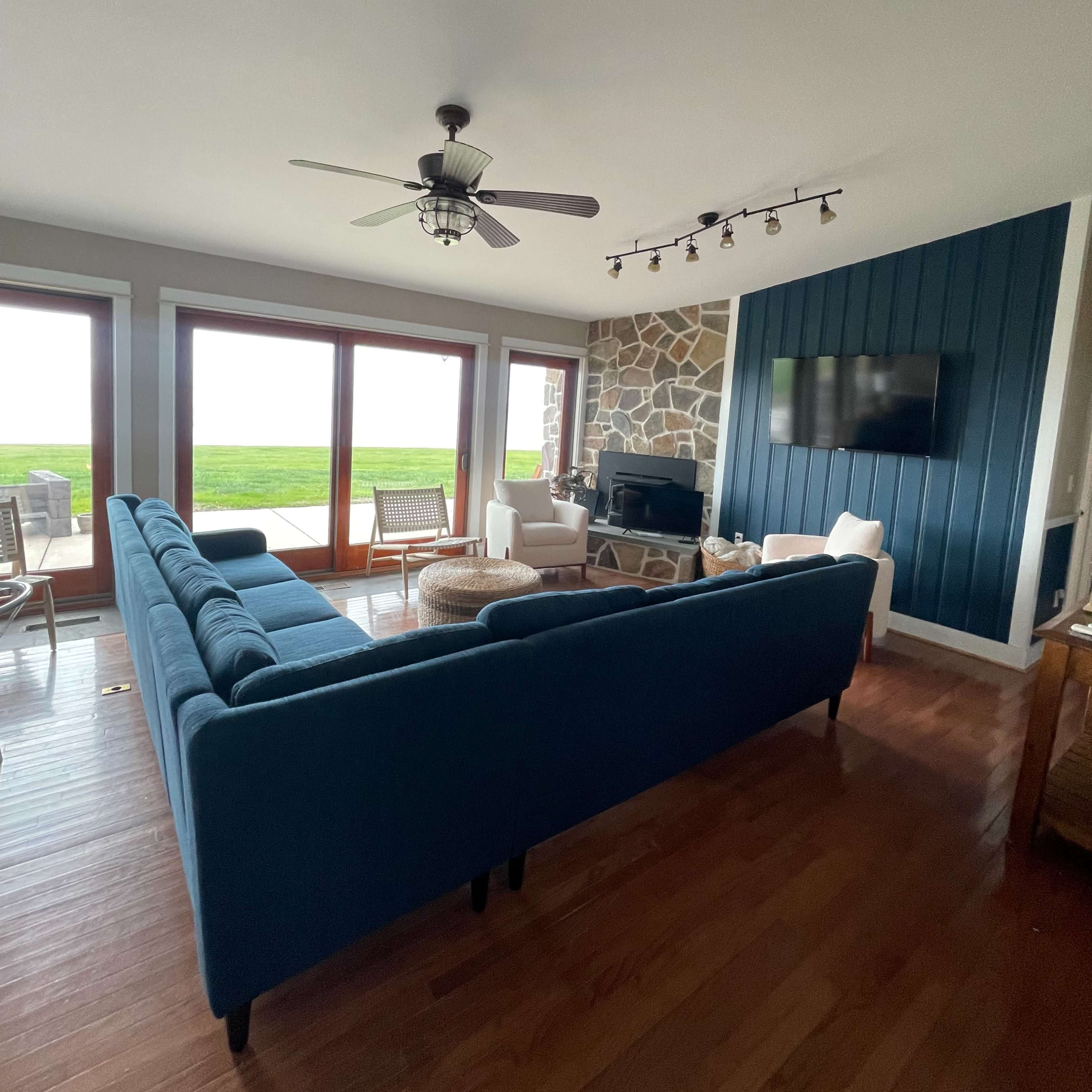 The living room features a blue sofa, a stone accent wall, and large windows with a view of the outdoors.