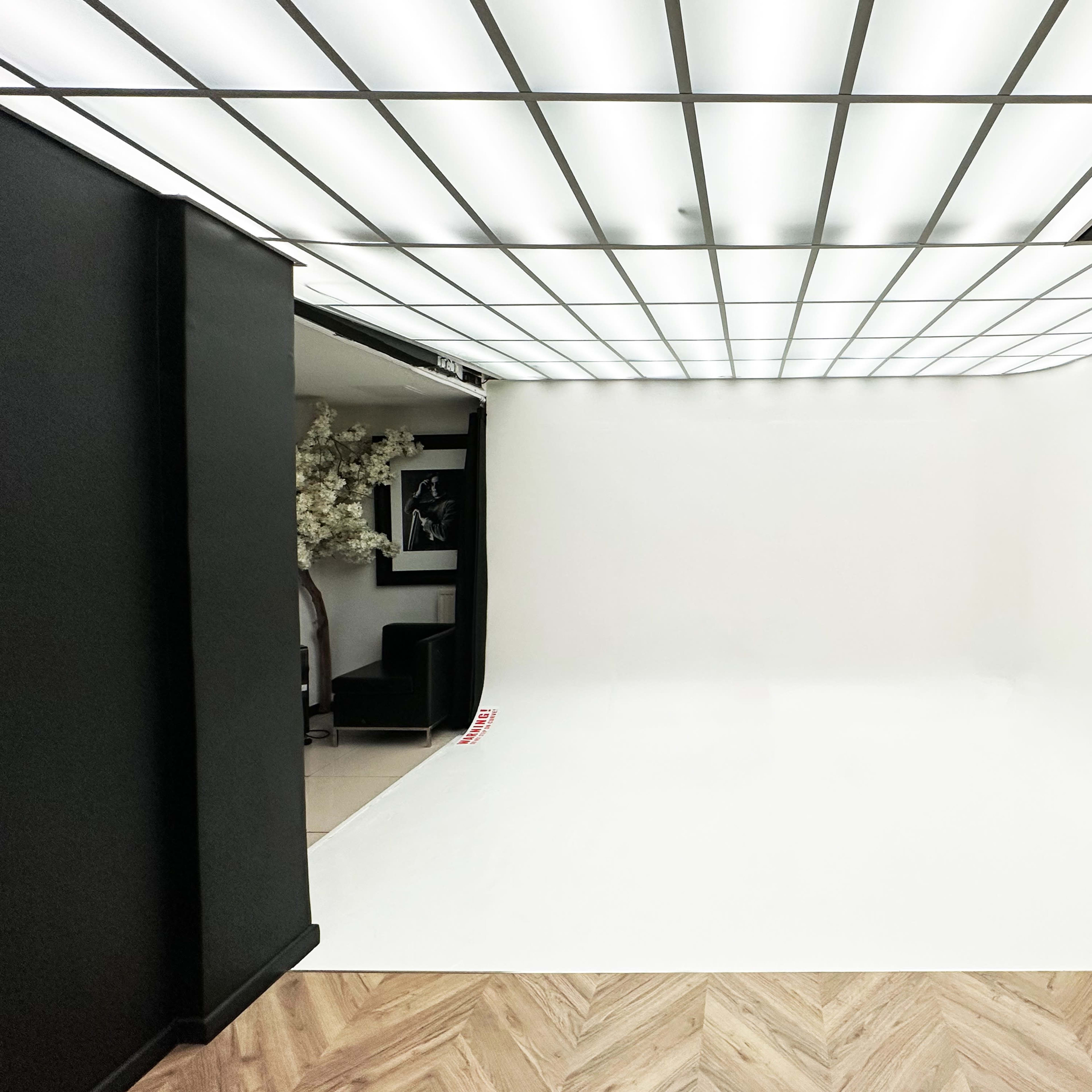 An empty photo studio features a seamless white backdrop and a grid-patterned overhead light.