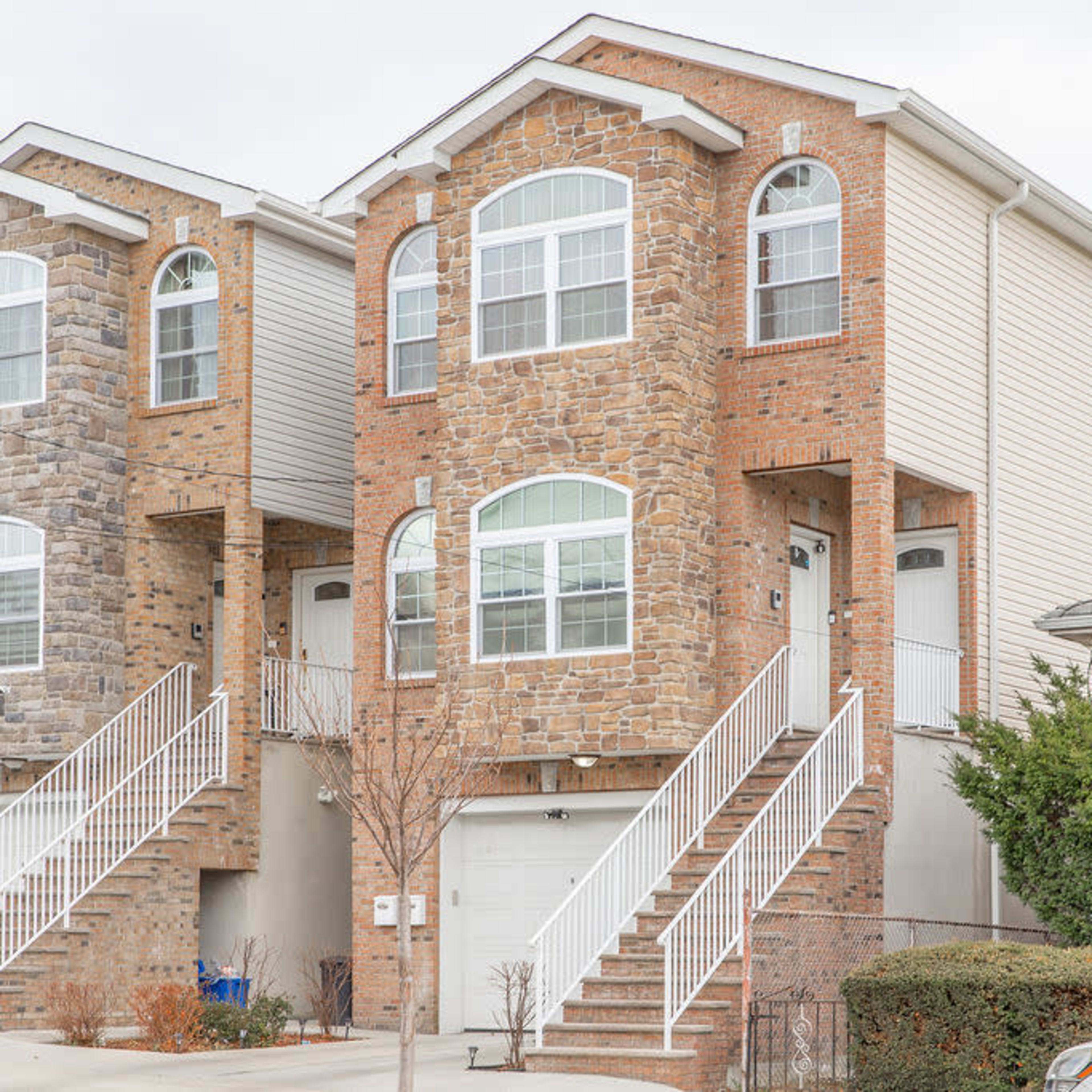 A two-family brick house with a stone facade, featuring separate entrances and staircases for each unit.