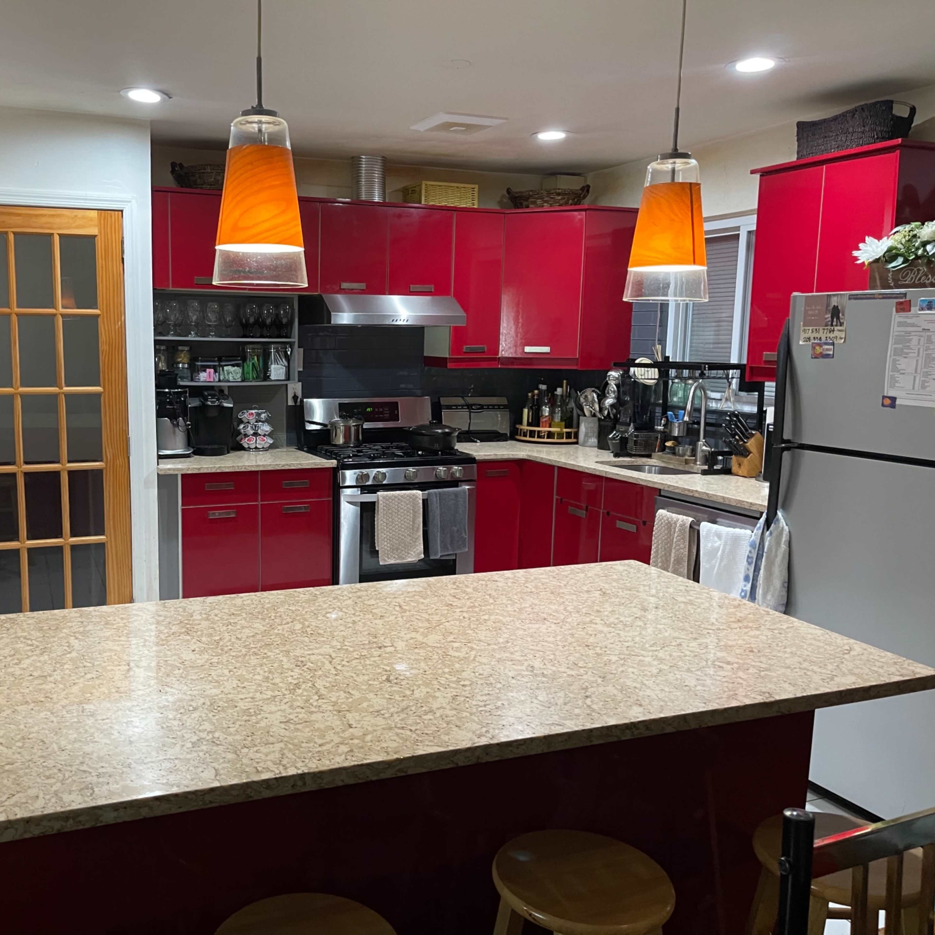 A modern kitchen features red cabinets, a granite countertop, and pendant lighting above the bar area.