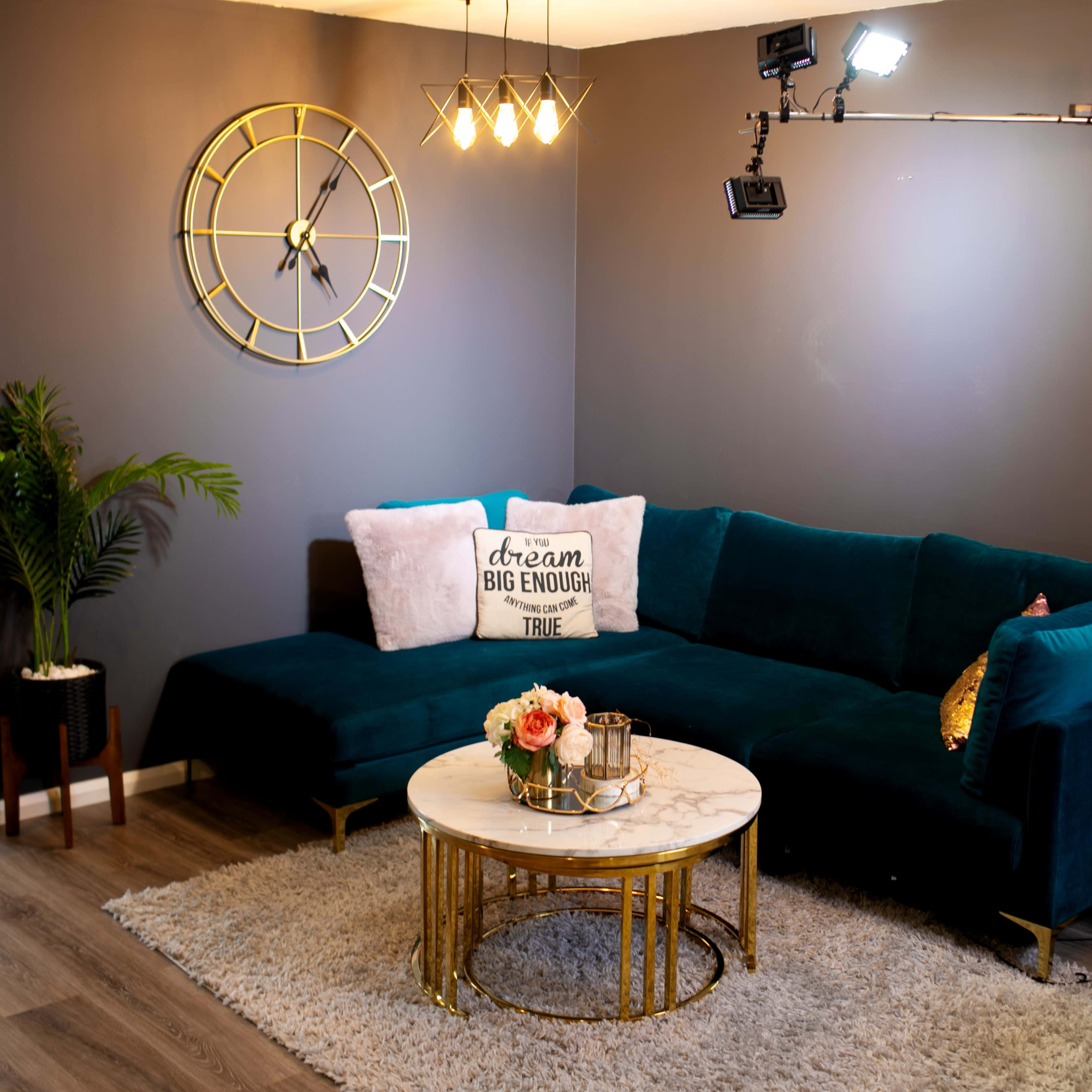 A cozy living room featuring a dark green sectional sofa, a round marble coffee table, and decorative elements like a clock and potted plants against a gray wall.