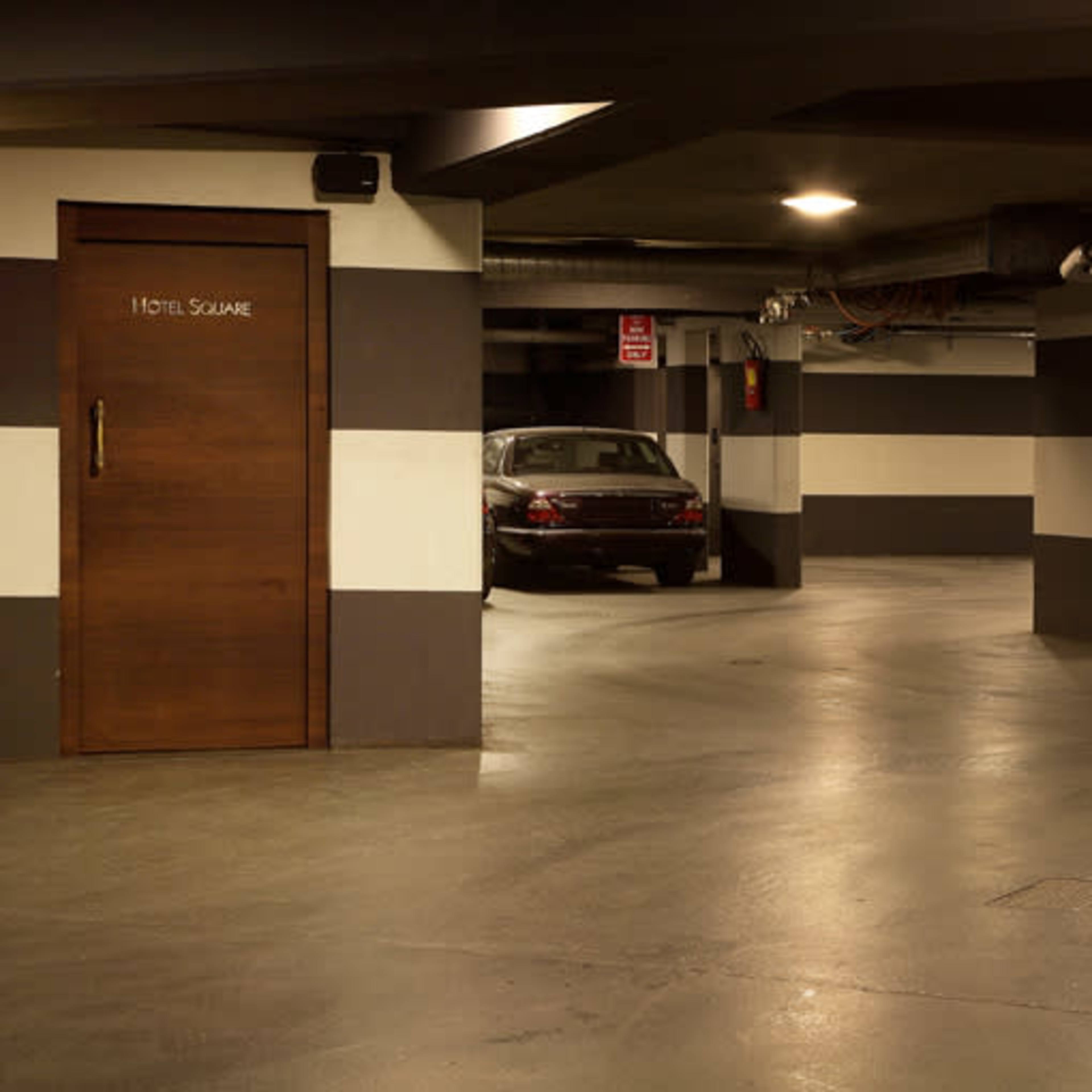 A dimly lit underground parking garage with striped walls and a parked car near a door labeled "HOTEL SQUARE."