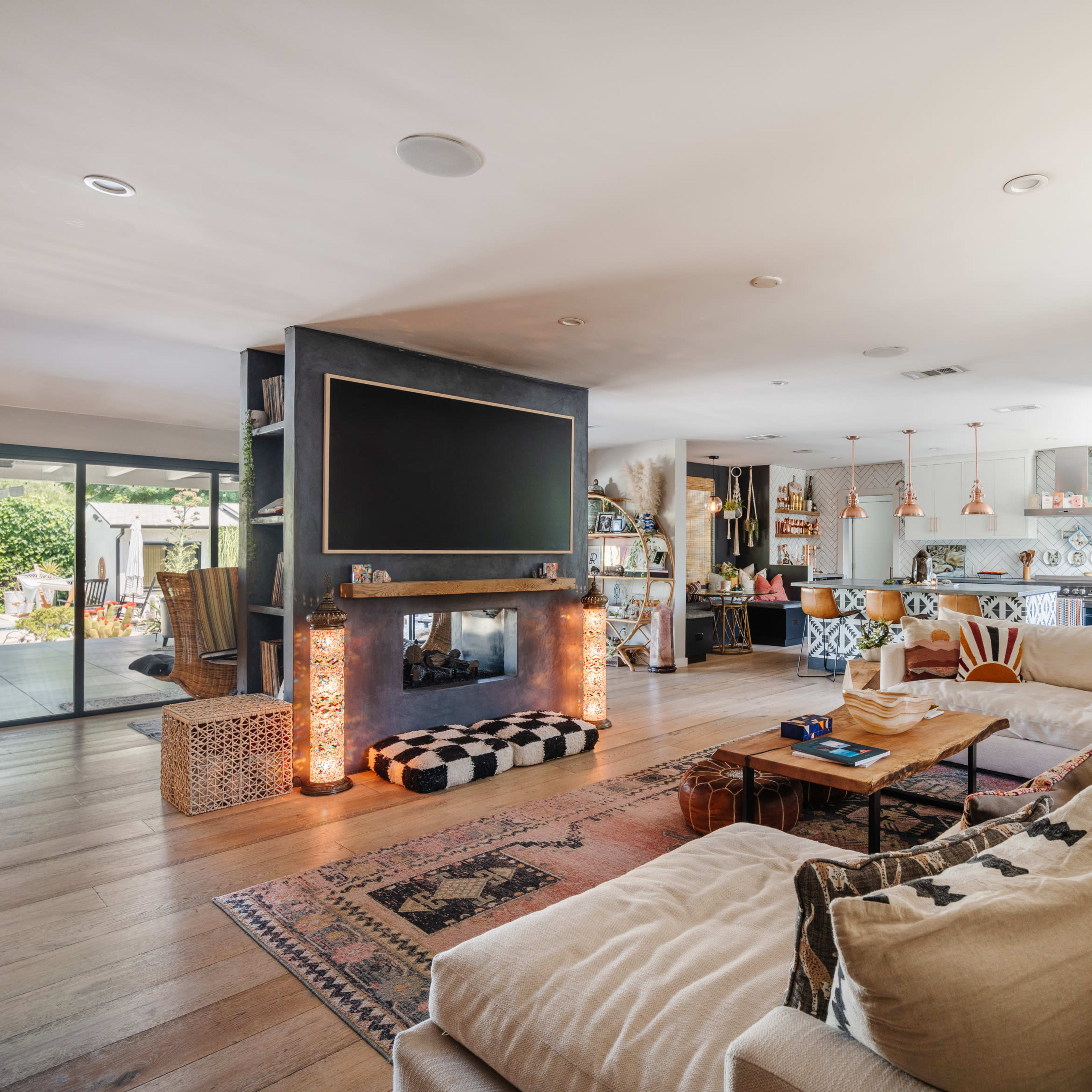 A spacious living room with a large television mounted on the wall, a cozy sectional sofa, and an open kitchen area visible in the background.