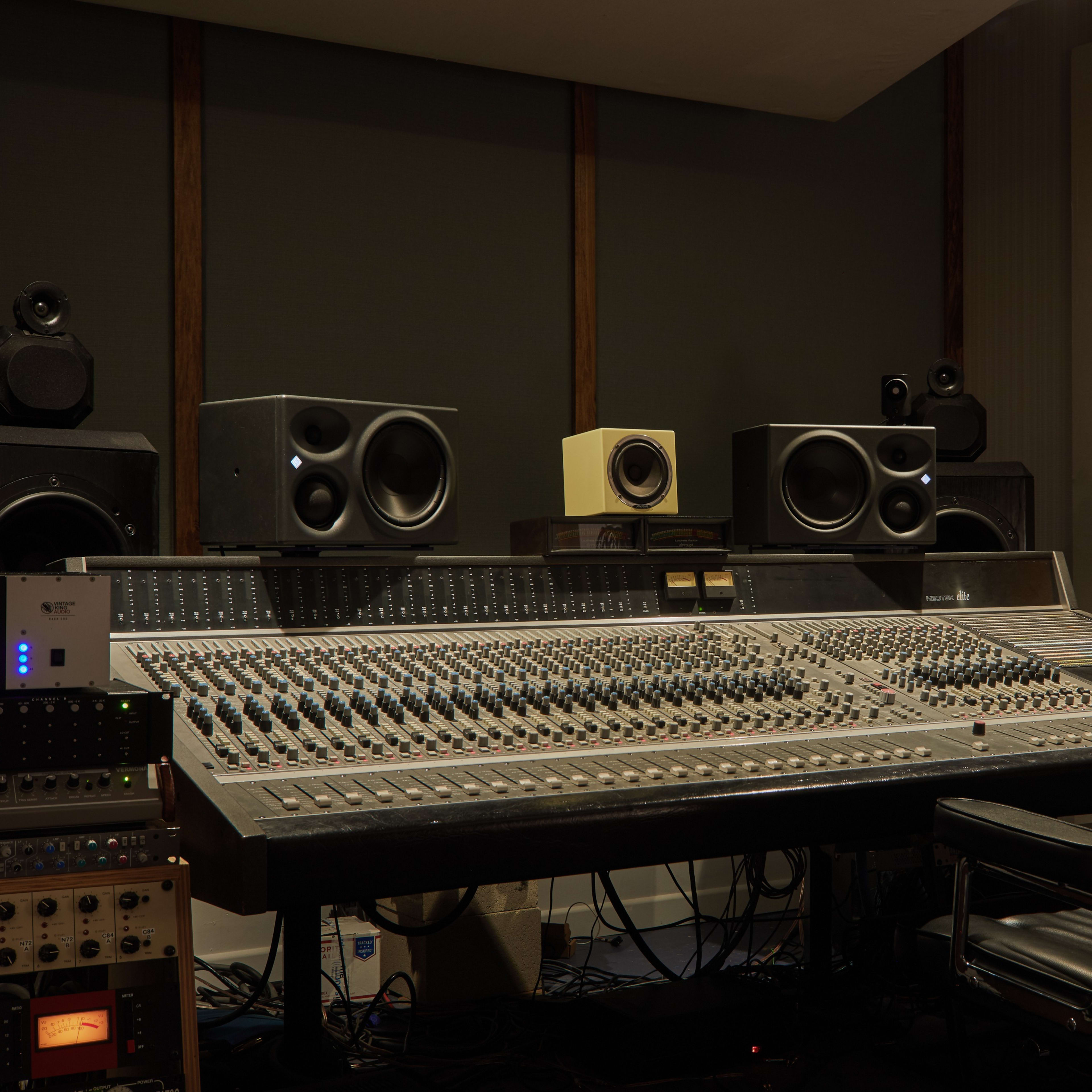 A recording studio features a large mixing console surrounded by speakers and audio equipment.
