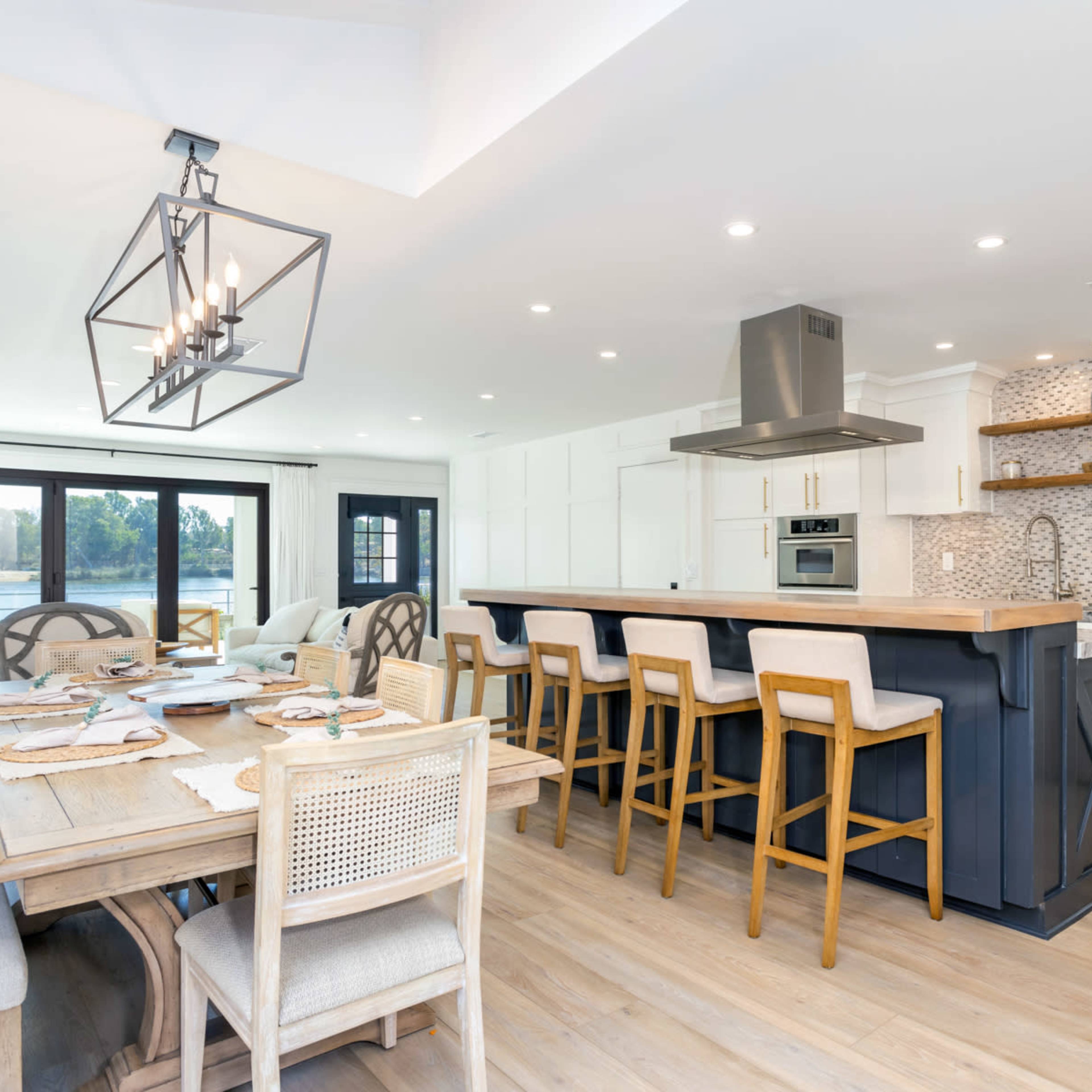 A modern kitchen and dining area feature a large island with bar seating, stainless steel appliances, and a table set for a meal.