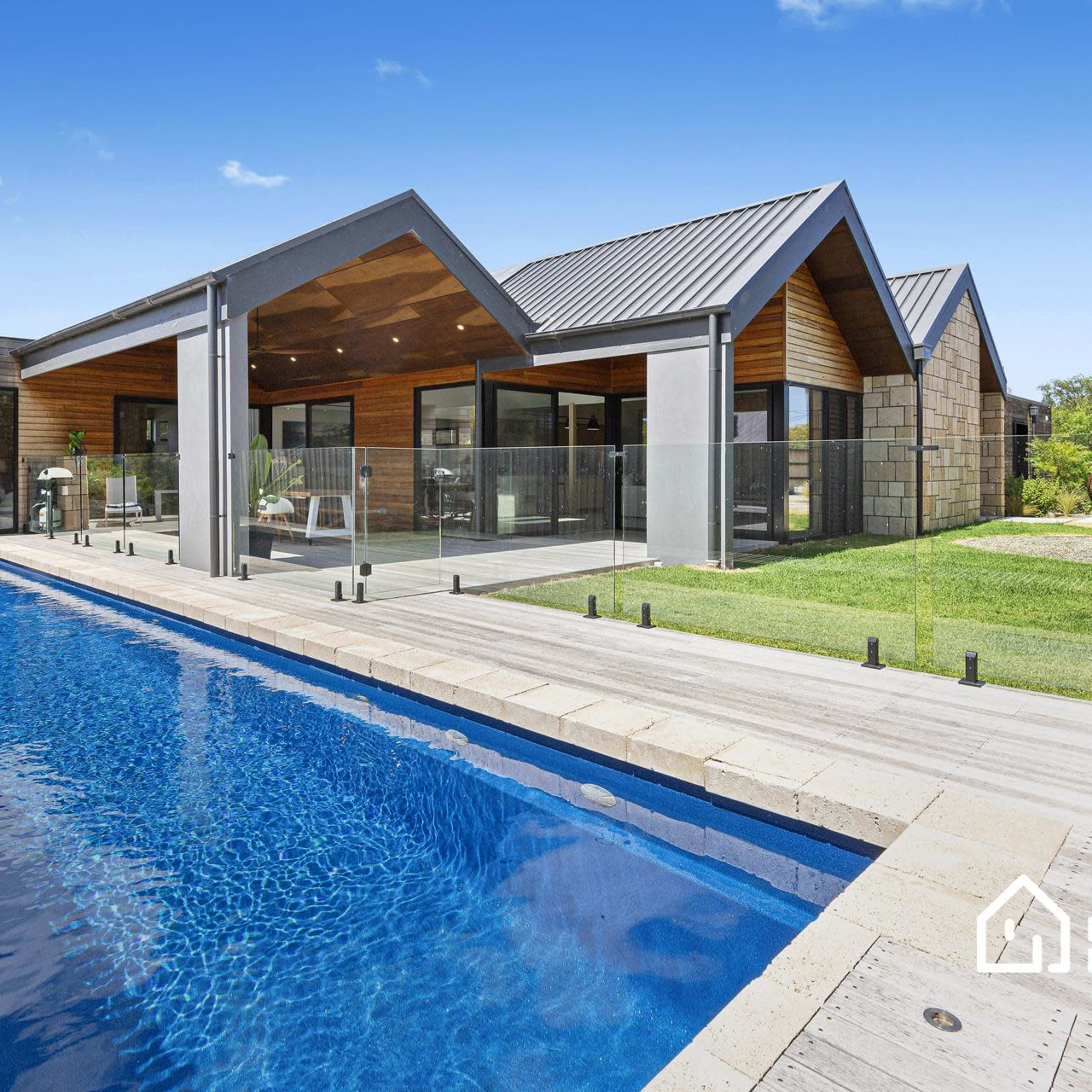 A modern house with a swimming pool and a landscaped yard under a clear blue sky.
