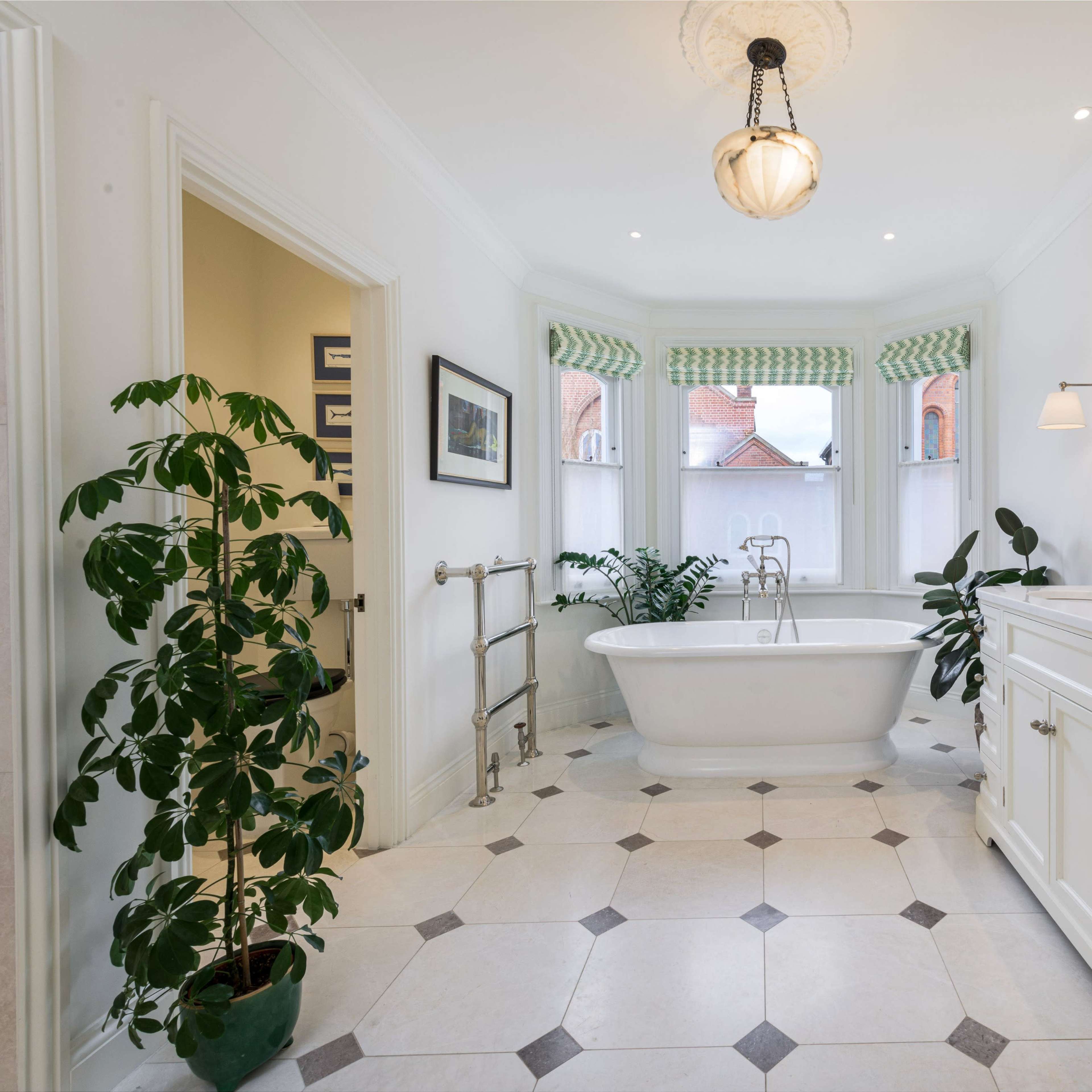 The spacious bathroom features a freestanding tub, a double sink vanity, and large windows with green patterned shades.