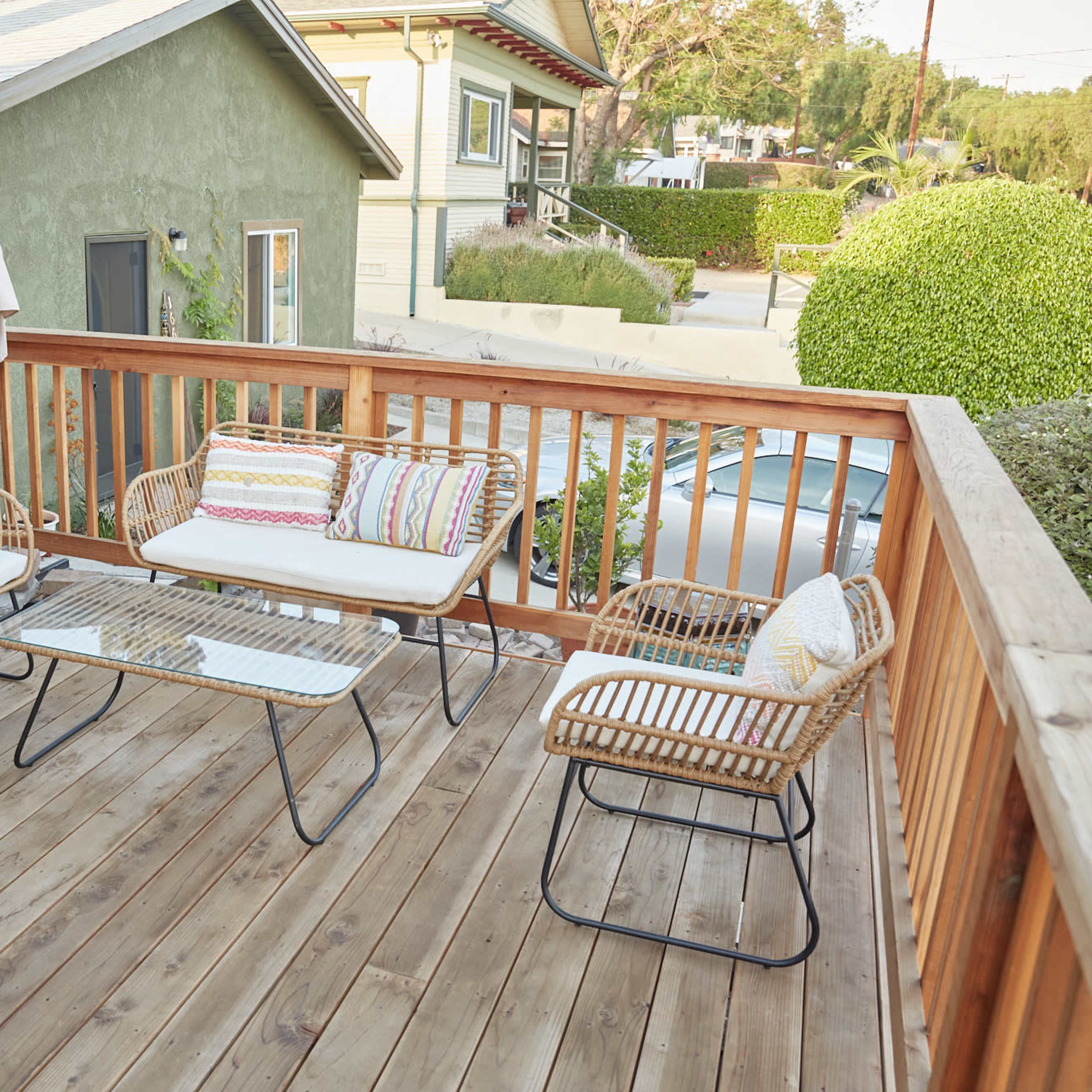 A wooden deck furnished with a glass-top coffee table and four rattan chairs, each with decorative cushions.