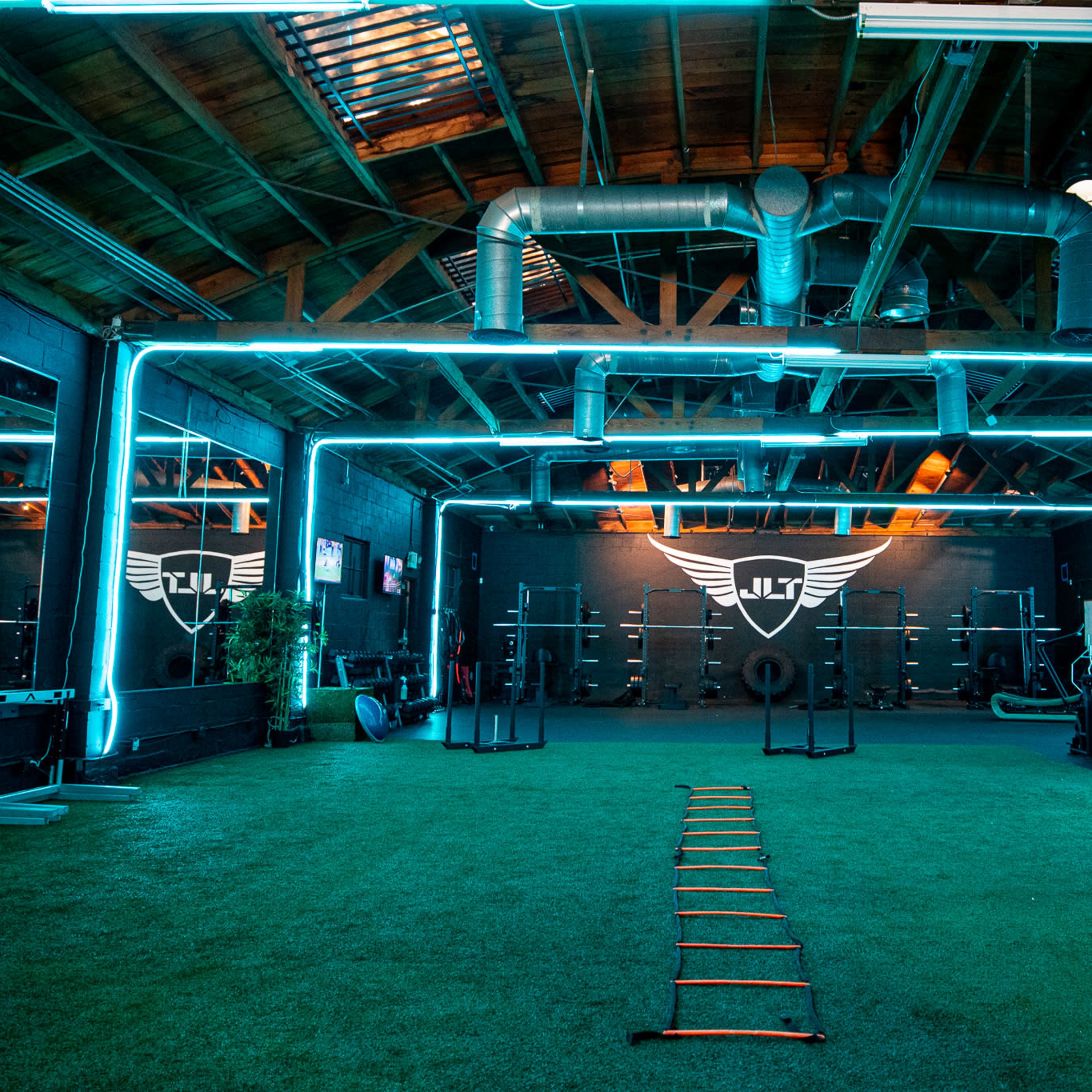 A gym interior features green turf flooring, neon blue lighting, and various exercise equipment along the walls.