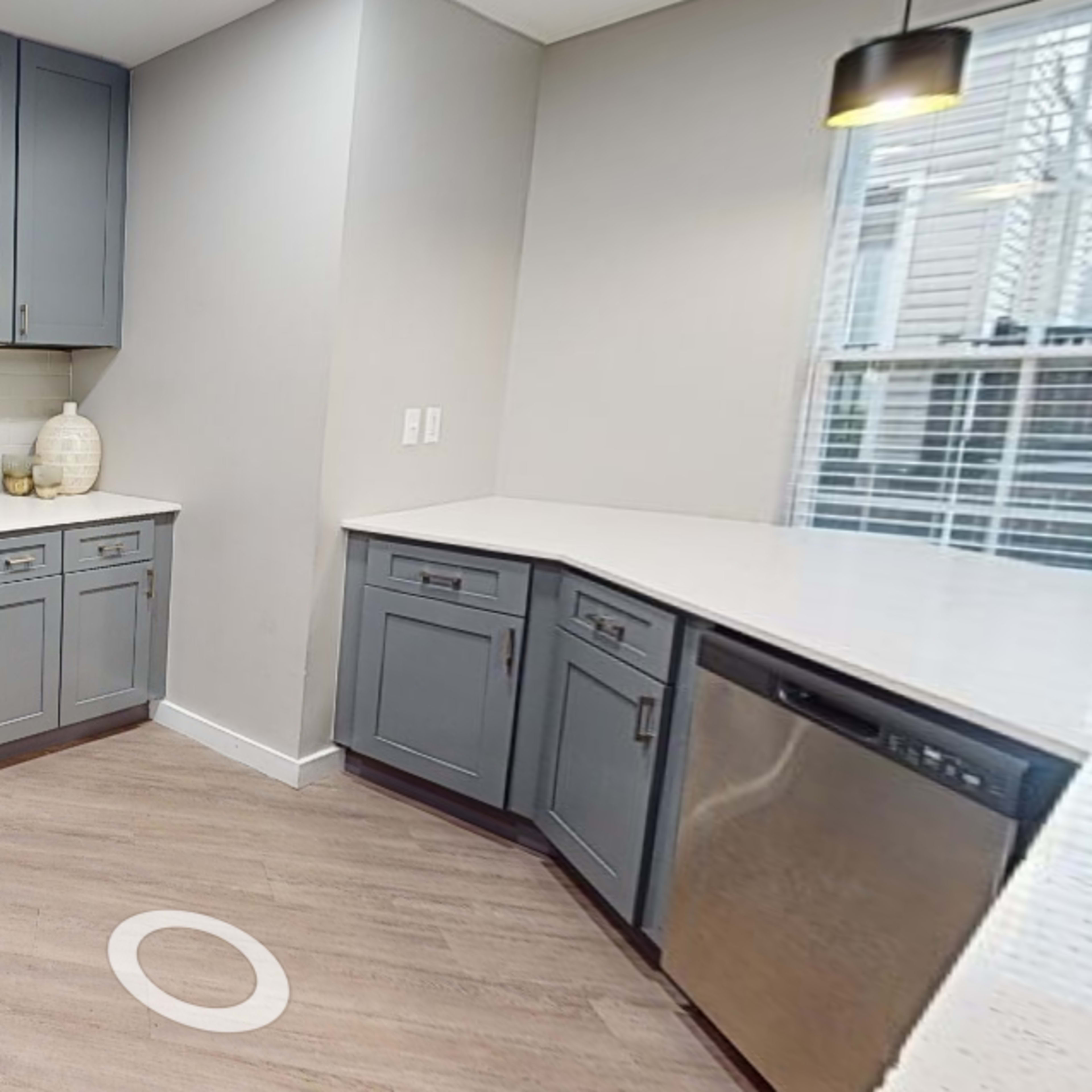 A modern kitchen with gray cabinetry, stainless steel appliances, and light-colored countertops.